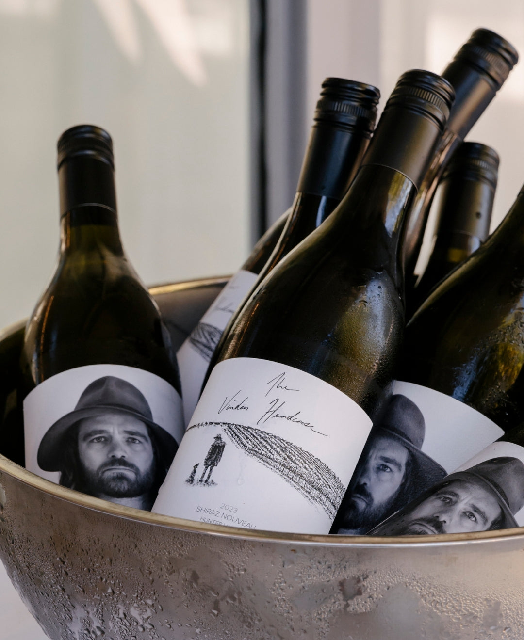 A selection of wine bottles in an ice bucket, each featuring a black-and-white portrait of a man wearing a hat on the labels.