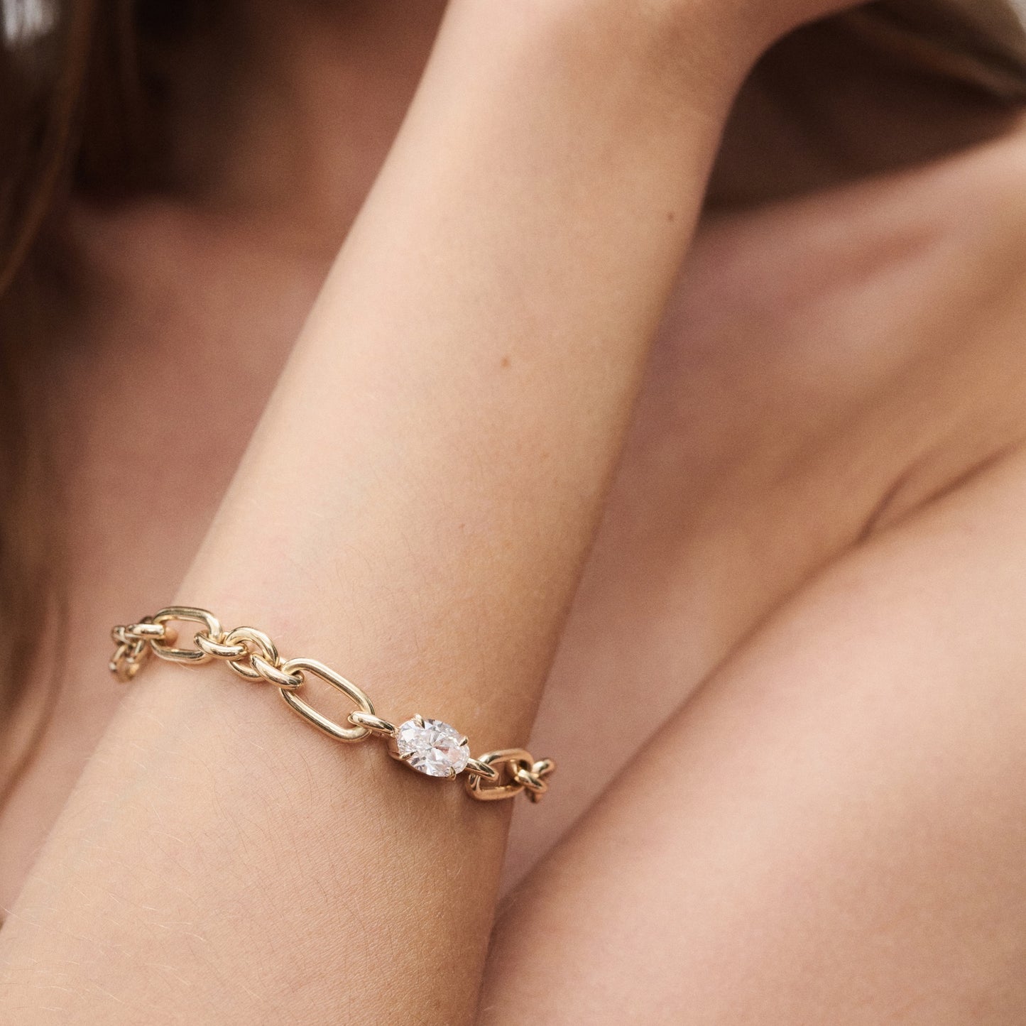 Gold chain bracelet with a large oval diamond, worn on a woman's wrist against bare skin. Elegant and luxurious jewellery detail.