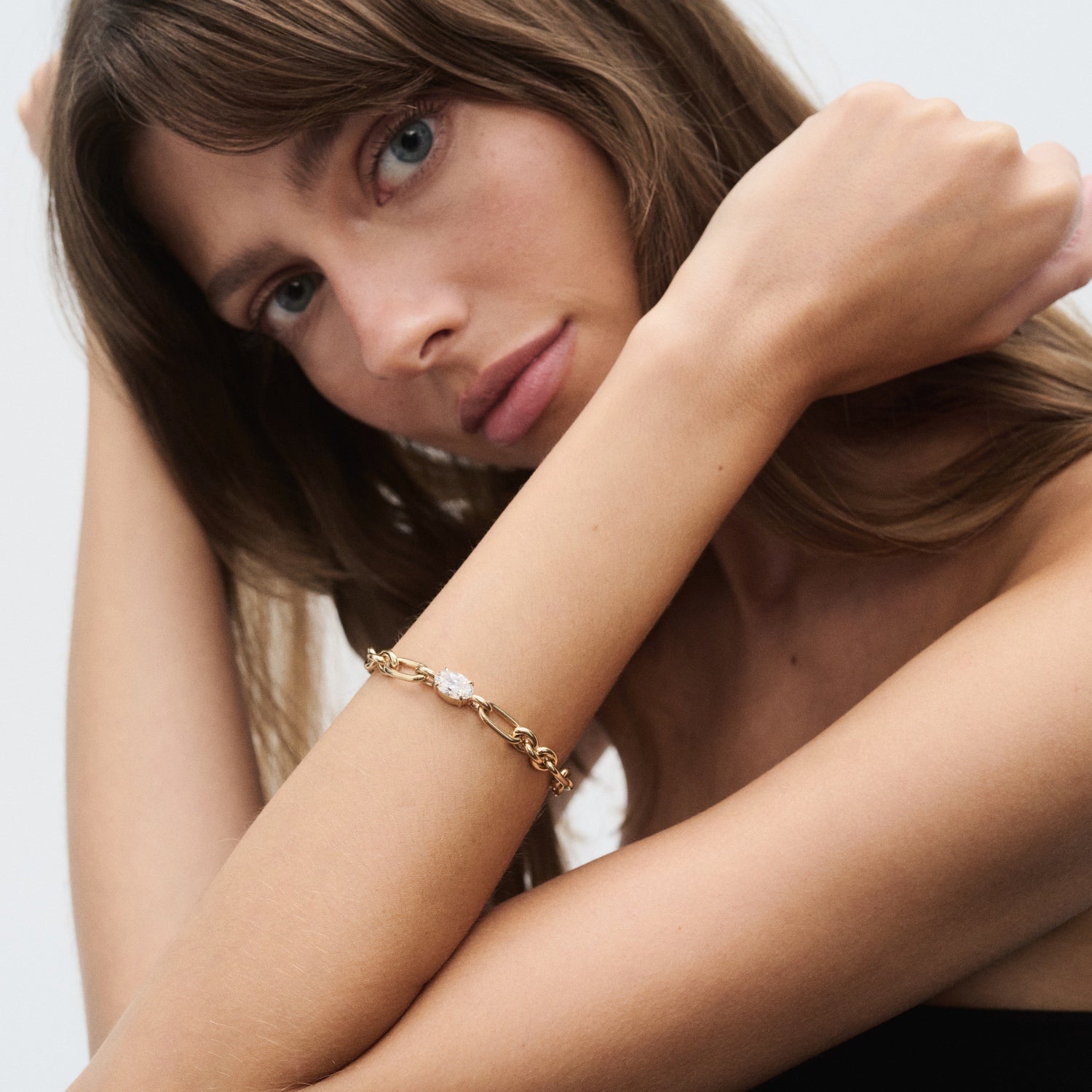 Woman with long hair wearing elegant gold bracelet, close-up. Minimalistic style, highlighting luxury jewellery. Neutral background.