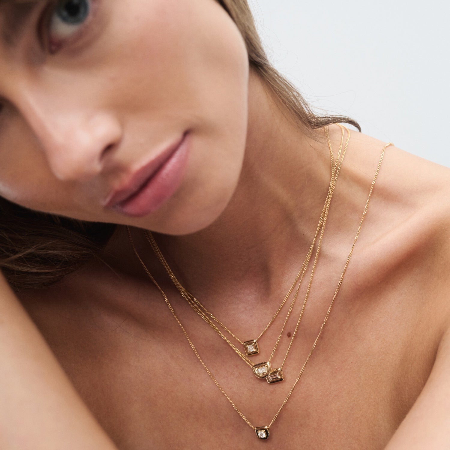 Model wearing layered gold necklaces with elegant square pendants, showcasing high-end luxury jewellery against a soft-focus background.