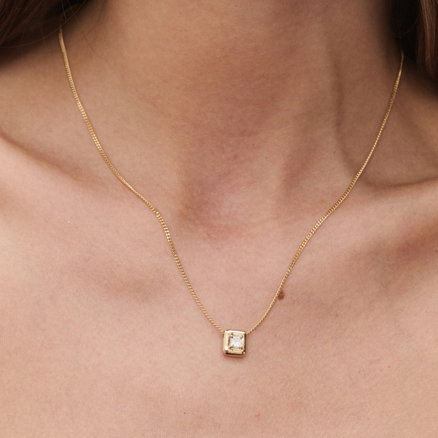 Close-up of a gold necklace with a square gemstone pendant, elegantly worn on a woman's neck. Luxurious jewellery design.