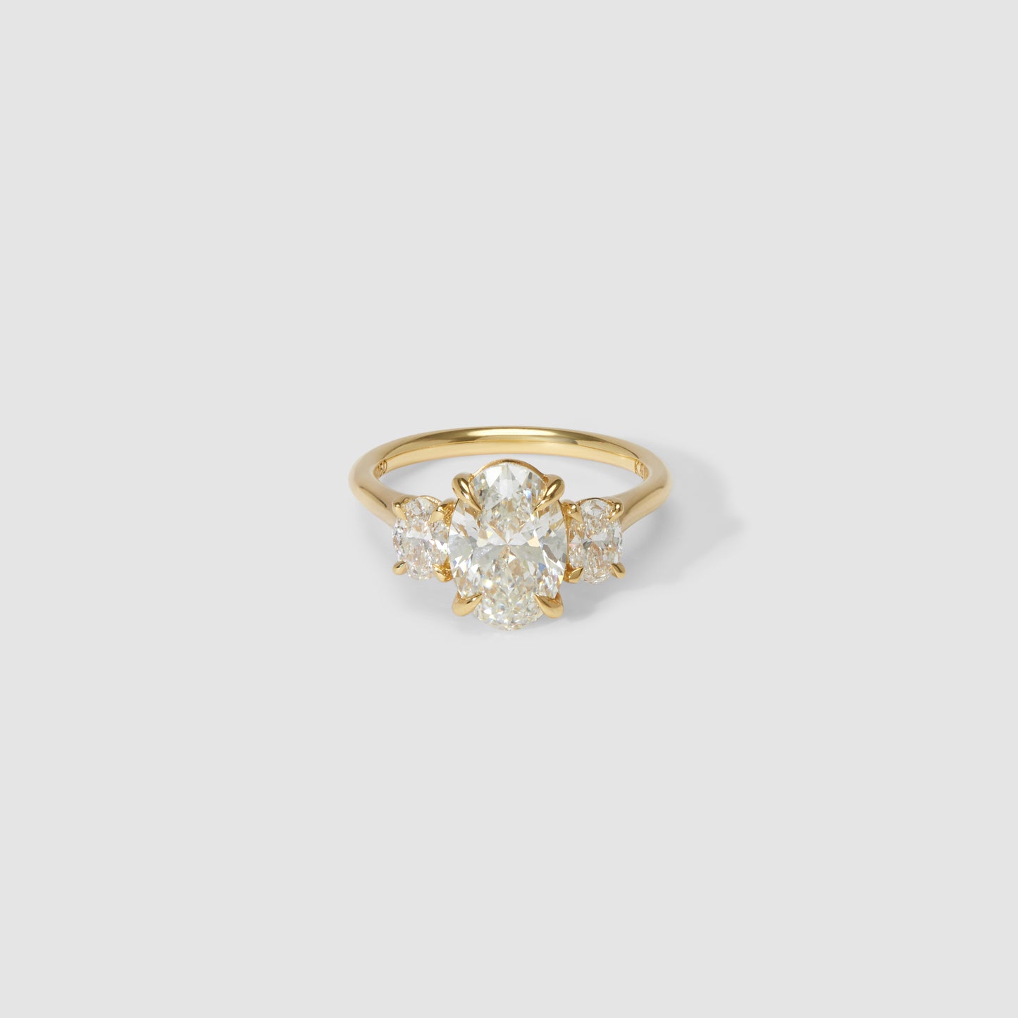Gold ring with a large, oval-cut diamond centre stone, flanked by two smaller diamonds, set in a polished band on a plain white background.