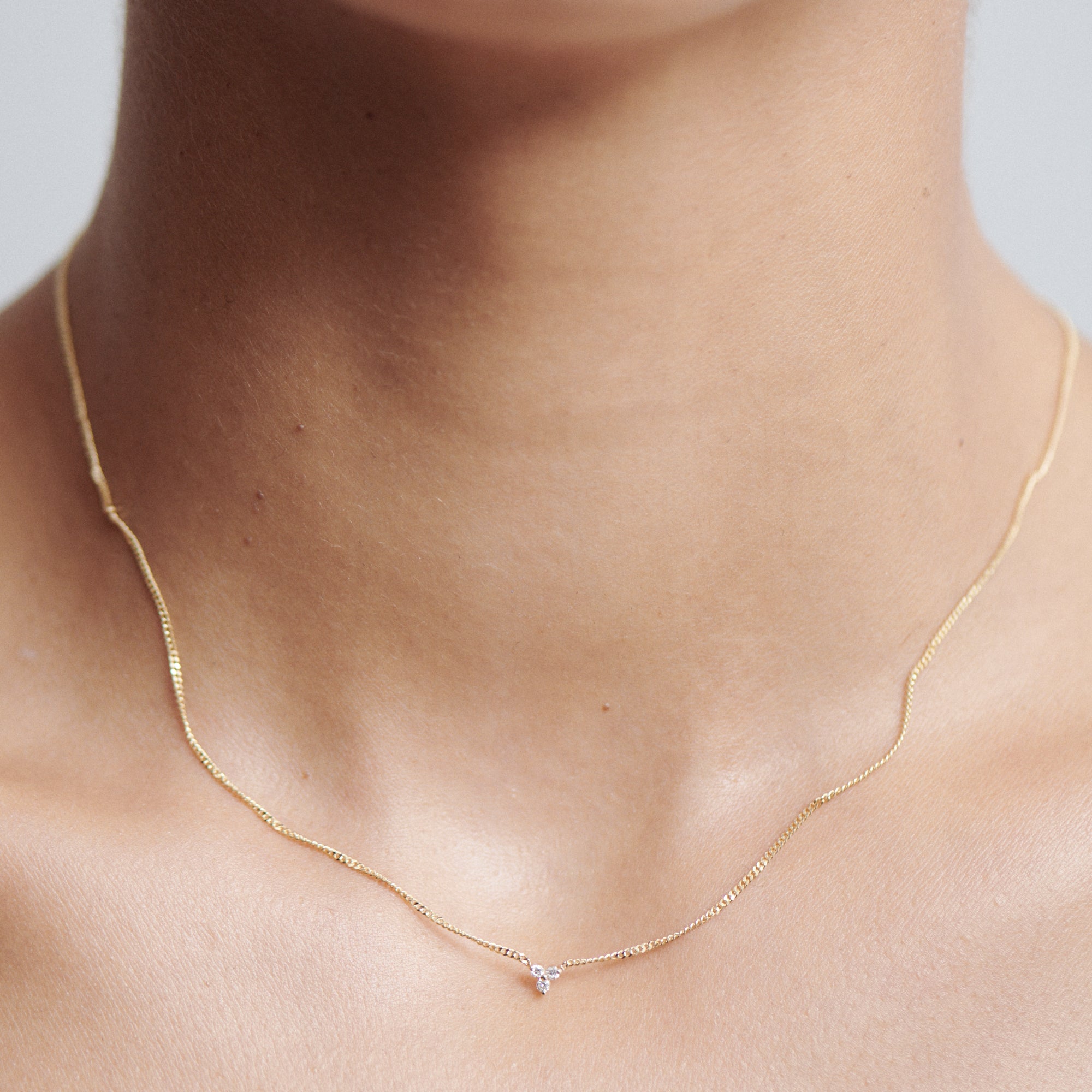 Close-up of a delicate gold necklace with a small diamond pendant on a person's neck; minimalist luxury jewellery.