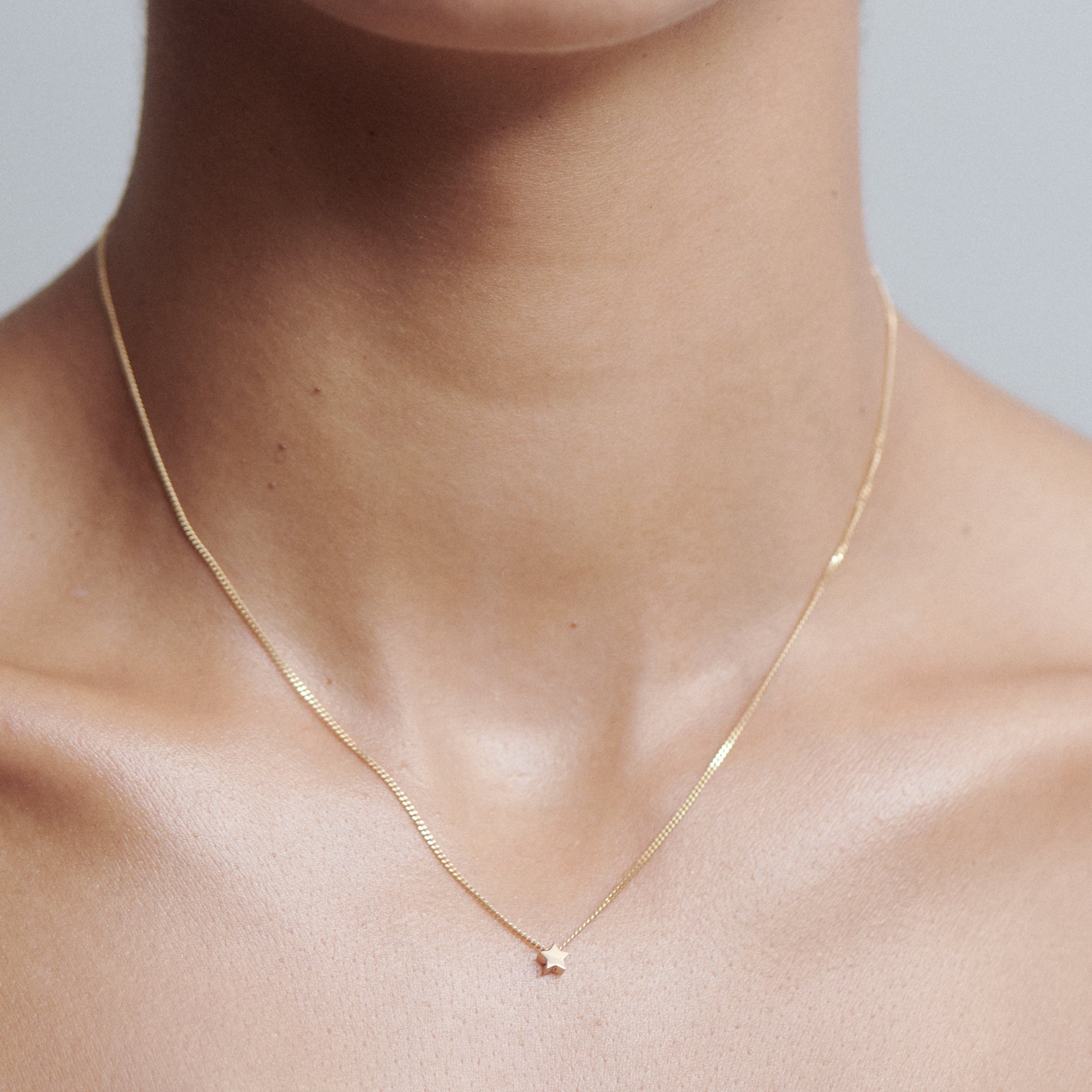 Gold necklace with a small star pendant on a person's neck, showcasing minimalist luxury jewellery style. Light background enhances elegance.