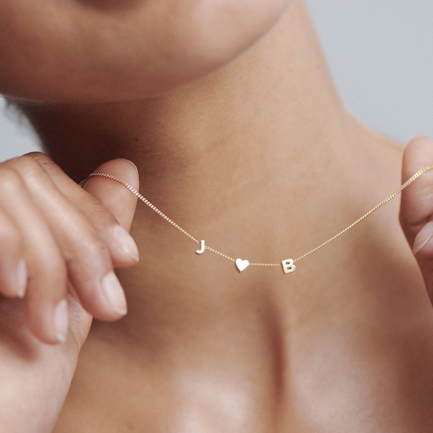 Woman holding delicate gold necklace with letter charms "J", heart, and "B". Perfect luxury jewellery for personal style.