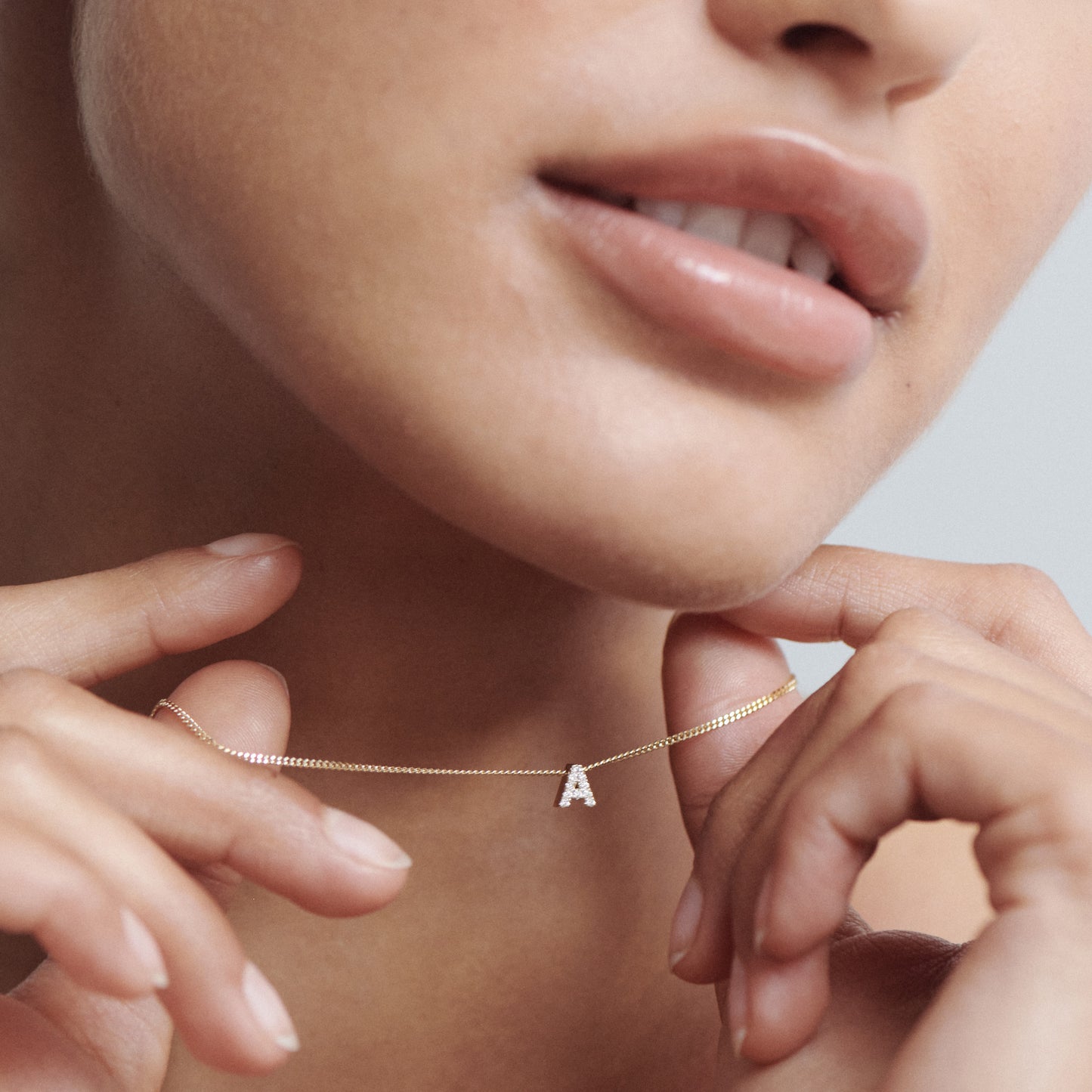 Woman holding a delicate gold necklace with a small, diamond-studded "A" pendant near her lips. Luxury jewellery close-up.

[text overlay: Sliding Diamond Letter Archive Charm on a 1.1mm Diamond Curb Chain (chain not included)]