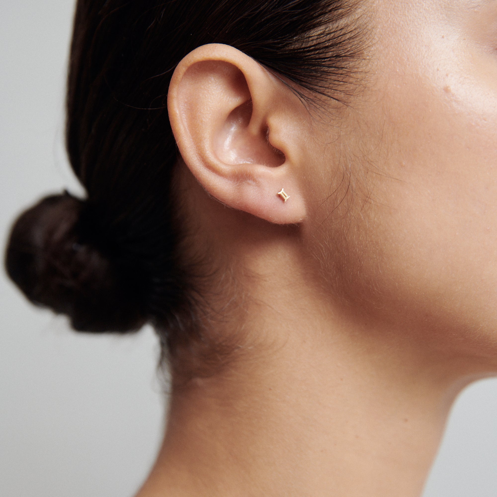 Close-up of a woman's ear with a minimalist gold star stud earring. Hair tied back, showcasing luxury jewellery elegance. [text overlay: Gemini] [text colour: #000000]