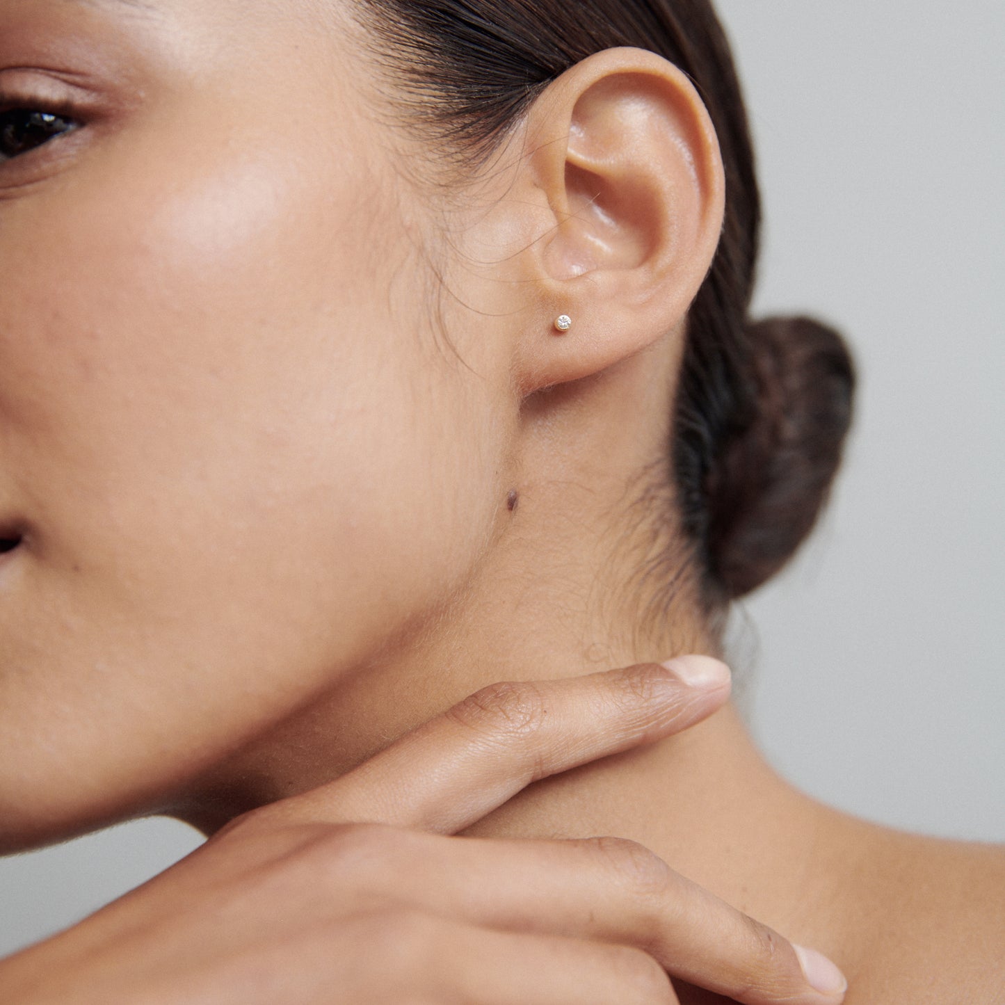 Close-up of a woman's ear wearing a small pearl stud earring. Her hand gently touches her neck. Elegant, minimalist jewellery style.
[text overlay: Small Size: 2mm or 0.03ct each]