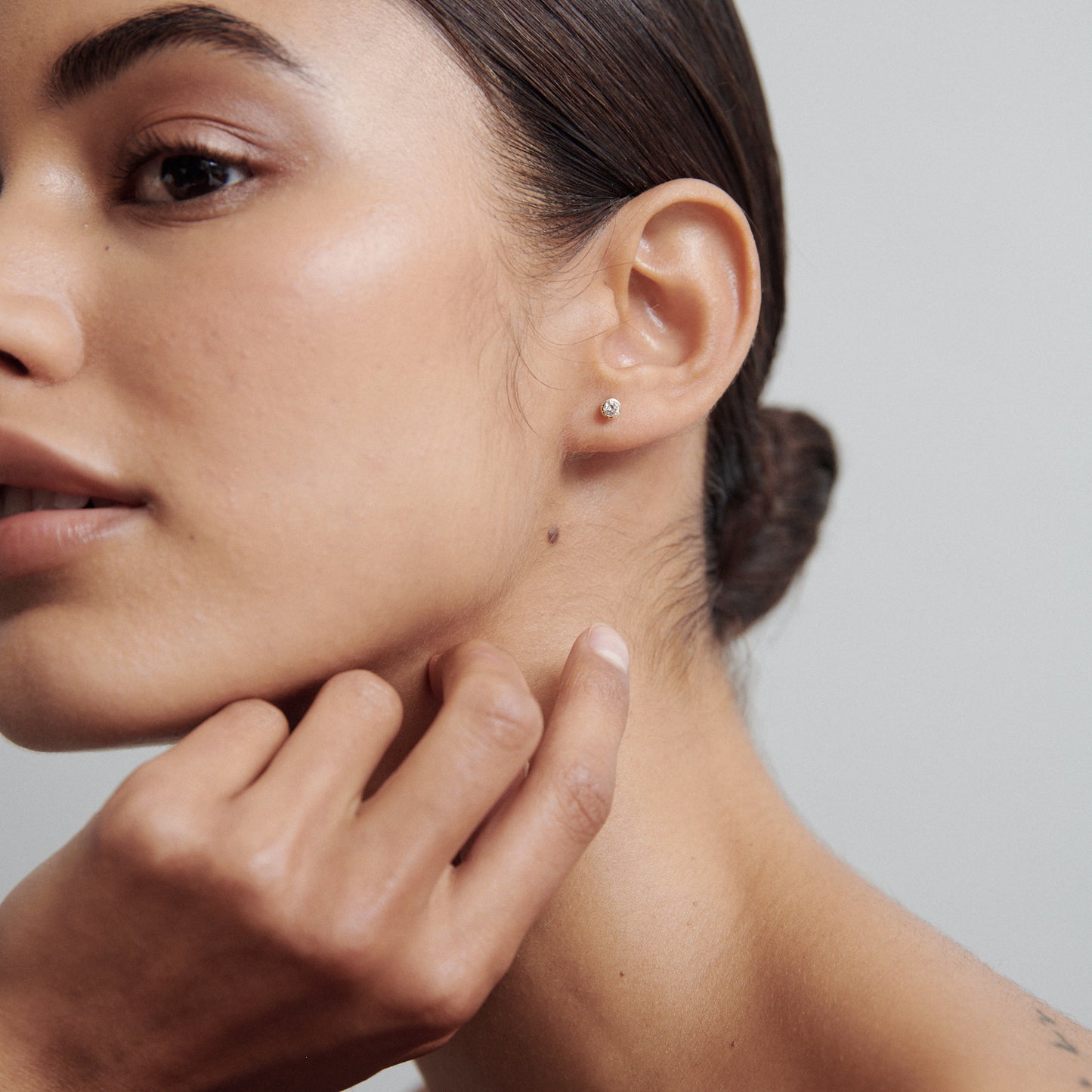 Close-up of a woman's face with a single diamond stud earring, smooth skin, and hair tied back neatly, touching her neck.
[text overlay: Medium Size: 3mm or 0.1ct each]