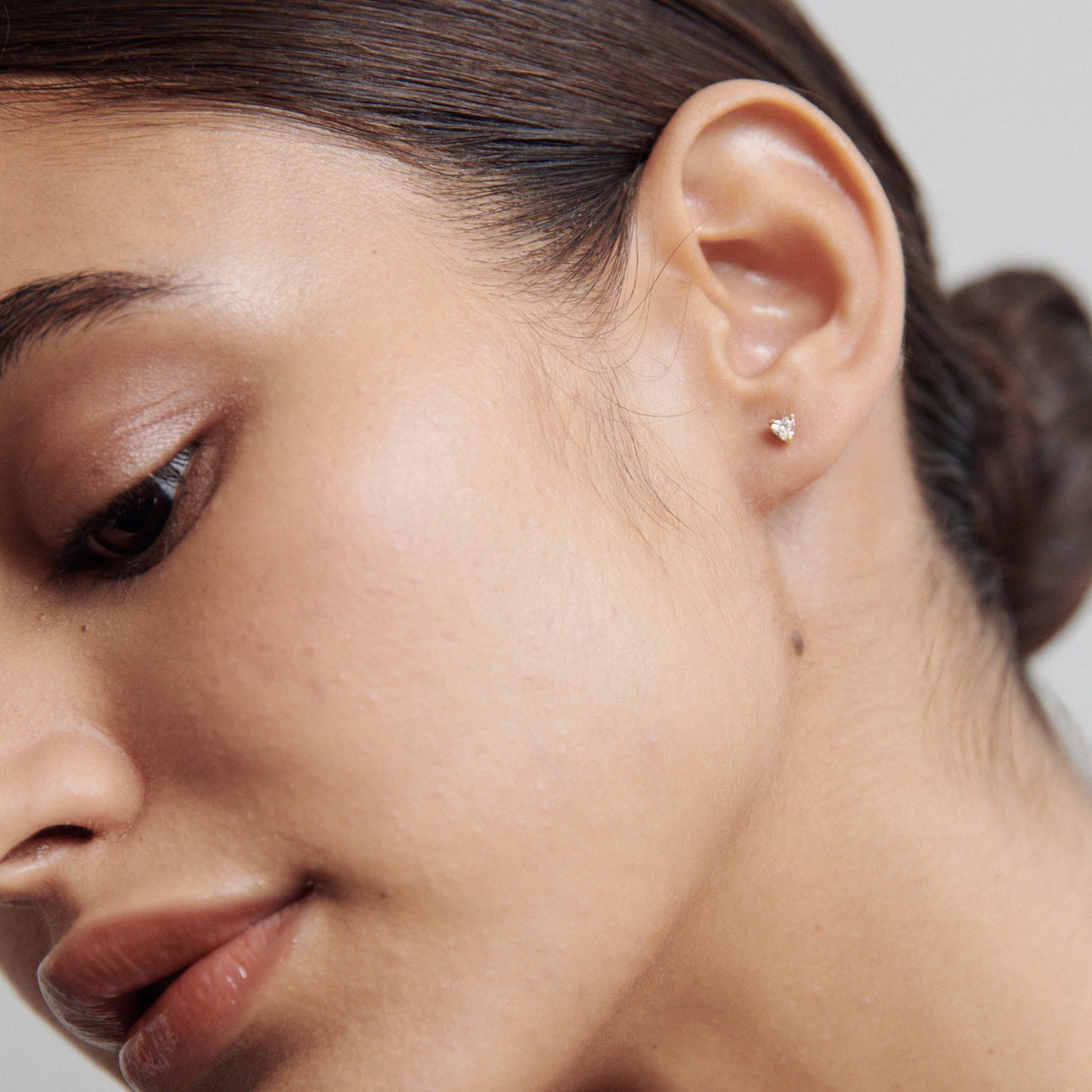 Close-up of a woman's ear adorned with a small, elegant diamond stud earring, emphasising luxury jewellery. Hair is pulled back neatly.