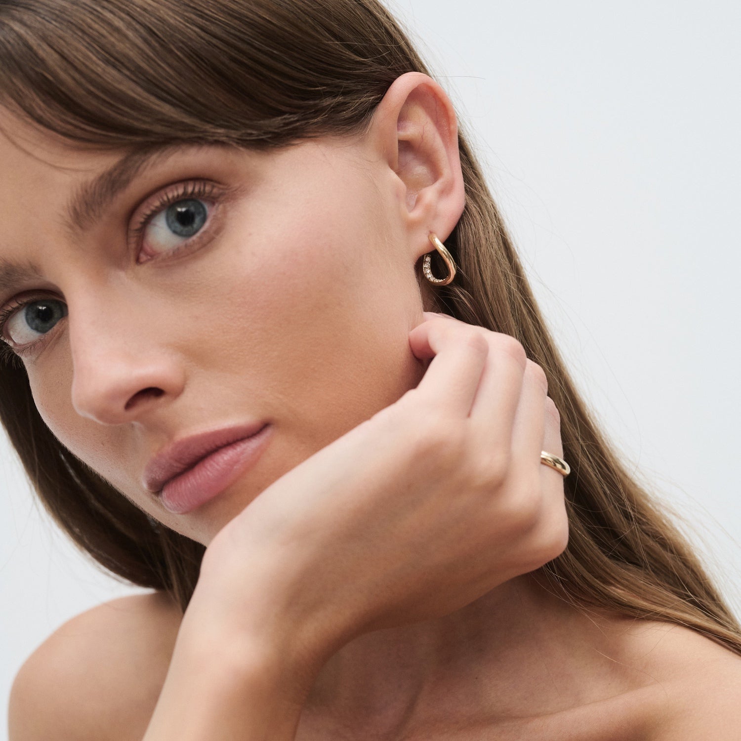Woman showcasing gold hoop earring and matching ring. Luxurious jewellery style against a minimalistic background.