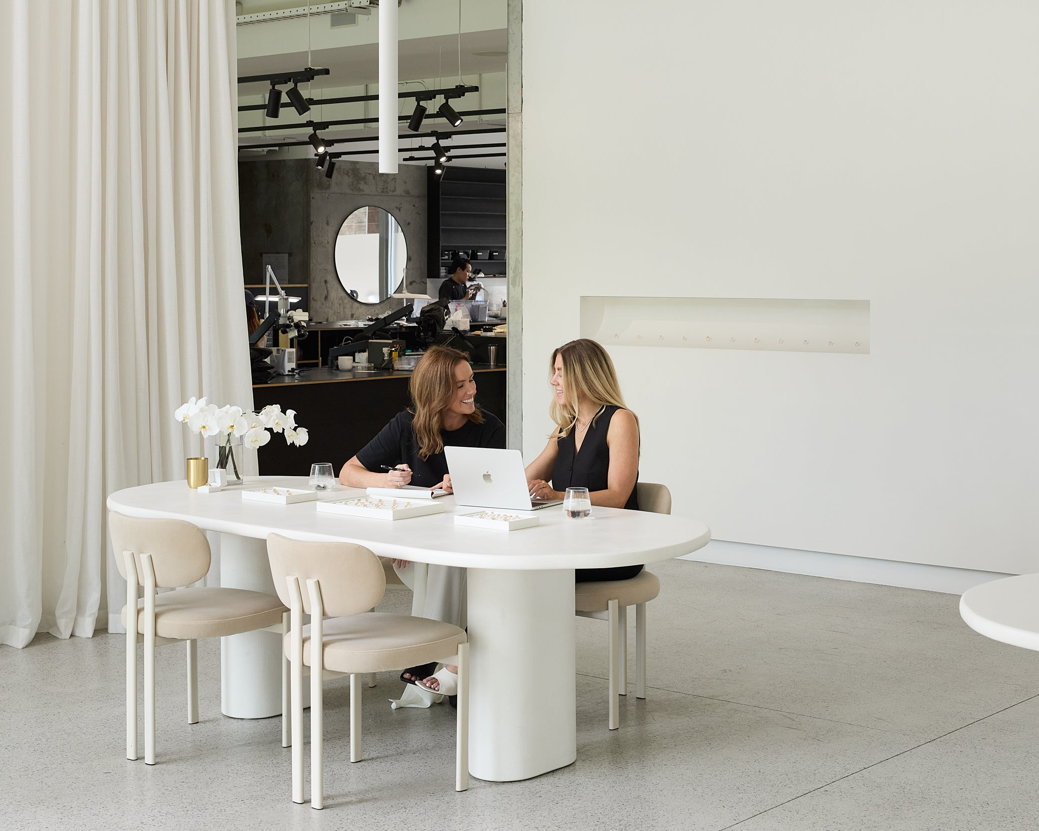 Kate & Kole founders, Sara and Maddy, sitting at a modern white dining table in a stylish interior setting.