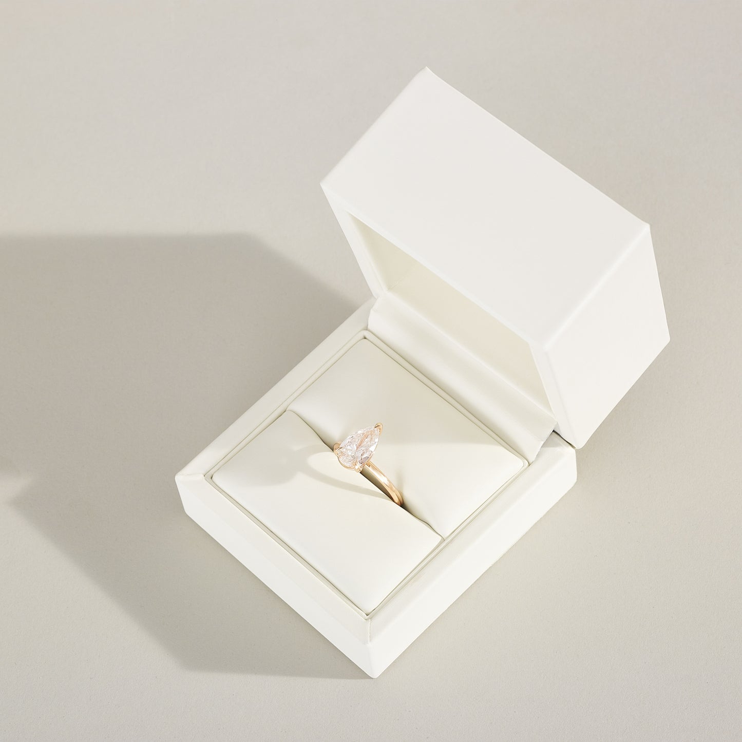 Gold ring with a diamond in an open white jewelry box on a light gray background