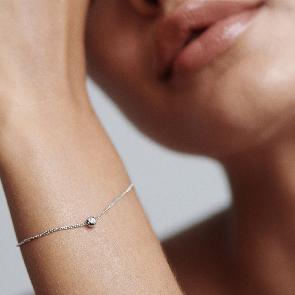 Close-up of a woman’s wrist with a delicate gold chain bracelet featuring a single diamond, set against her skin. Luxury jewellery elegance. [text overlay: ]