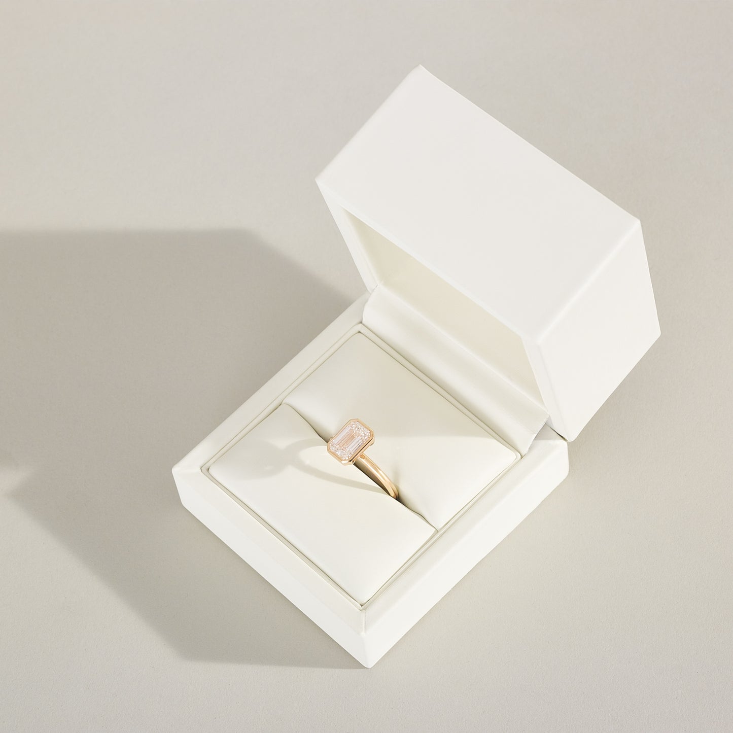 Gold ring in an open white jewelry box on a light gray background