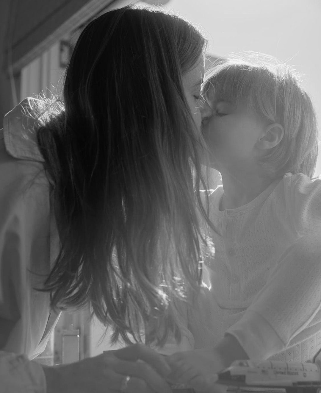 Mother and child share a tender kiss in a warmly lit room. The scene radiates love and intimacy, capturing a special family moment.