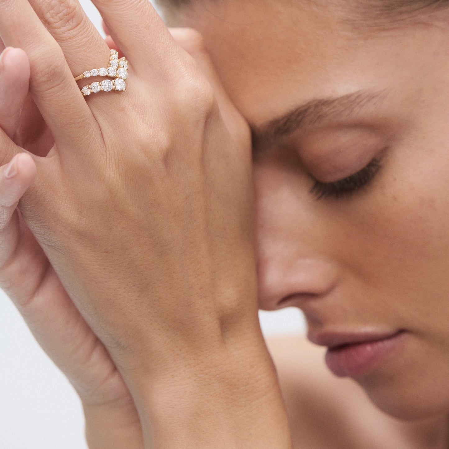 Woman with eyes closed, wearing an elegant gold ring adorned with sparkling diamonds, highlighting luxury jewellery craftsmanship.