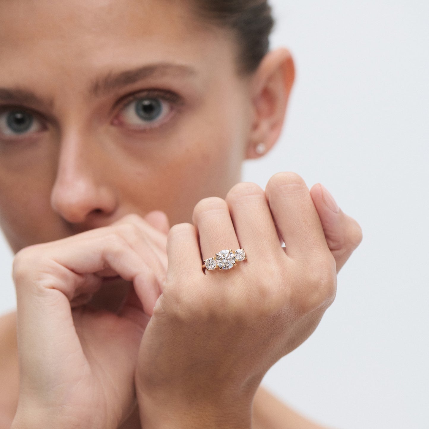 Woman showcasing a luxury diamond ring on her finger, set in a gold band, with a focused gaze in the background.