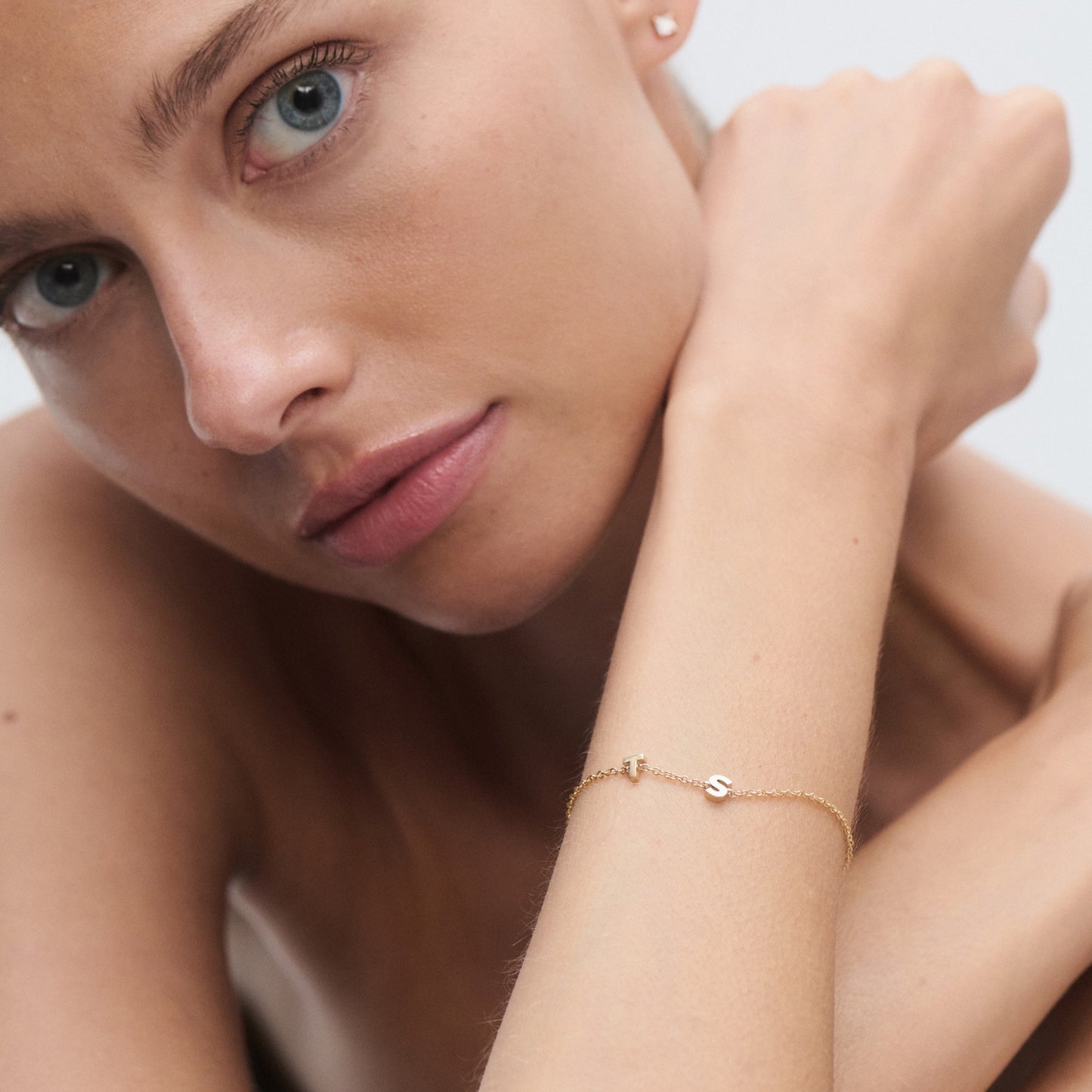 Close-up of a woman wearing a gold bracelet with initials "S" and "I", emphasising minimalist luxury jewellery.