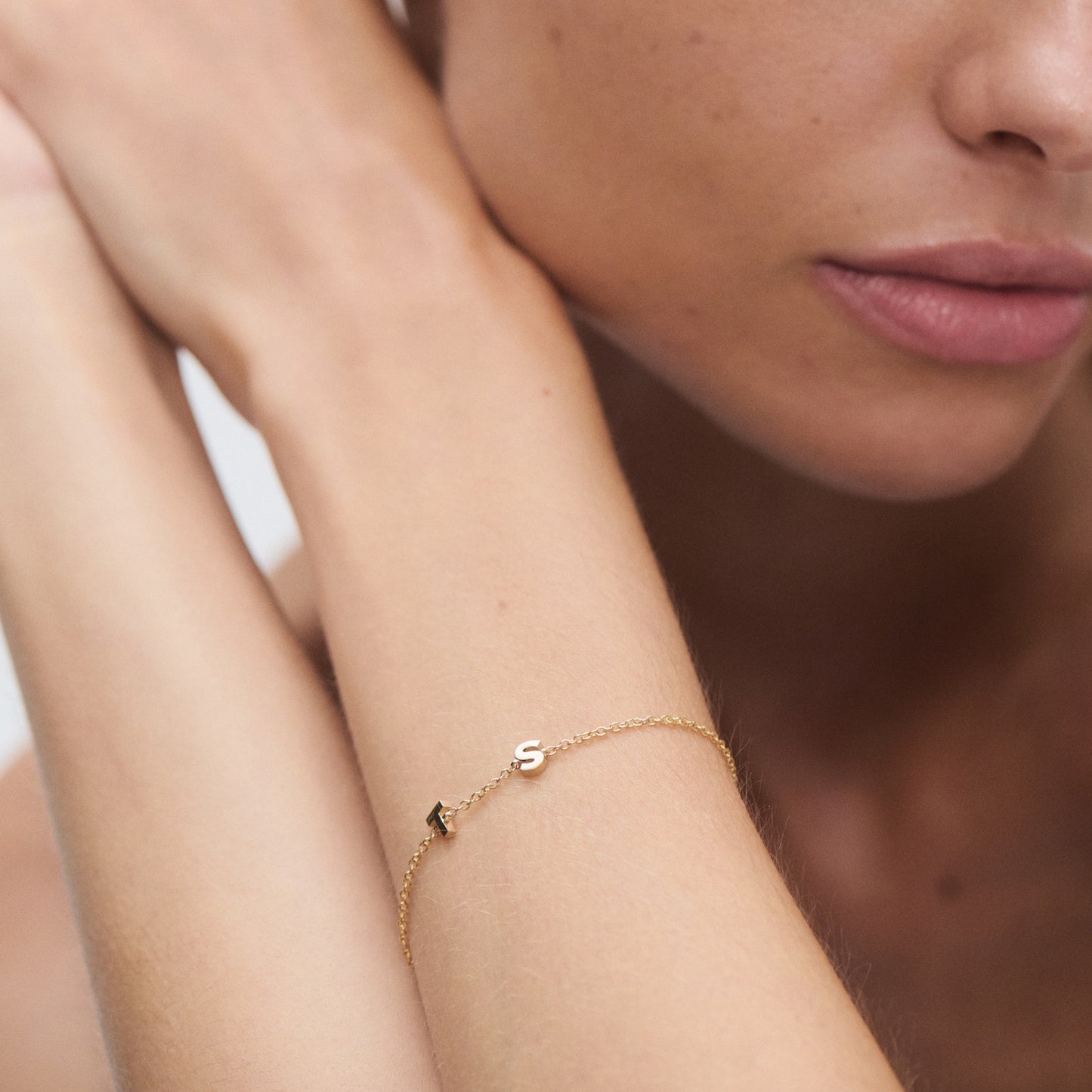 Close-up of a gold bracelet with an 'S' charm on a woman's wrist, highlighting minimalist luxury jewellery.