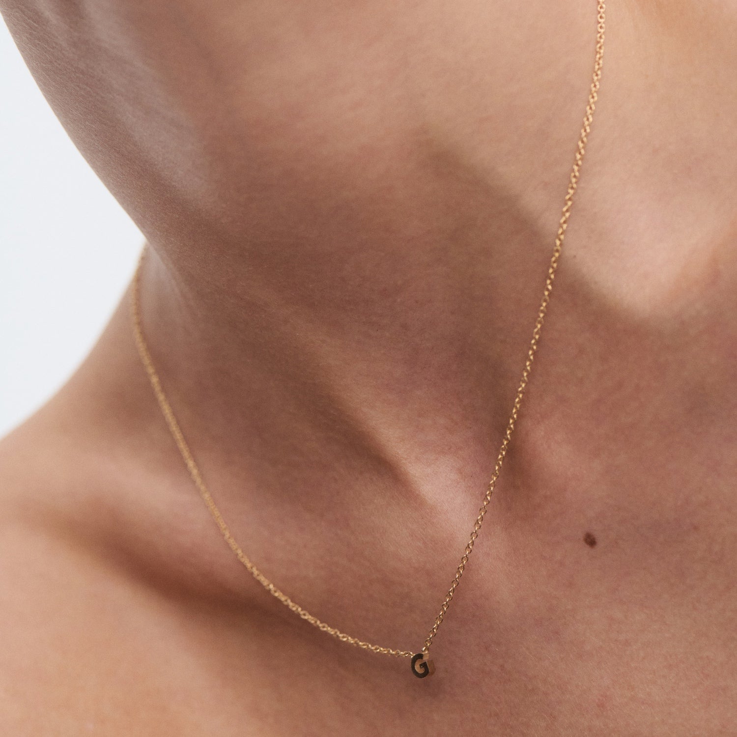 Close-up of a gold chain necklace with a small letter 'G' pendant on a person's neck, emphasising minimalist luxury jewellery.