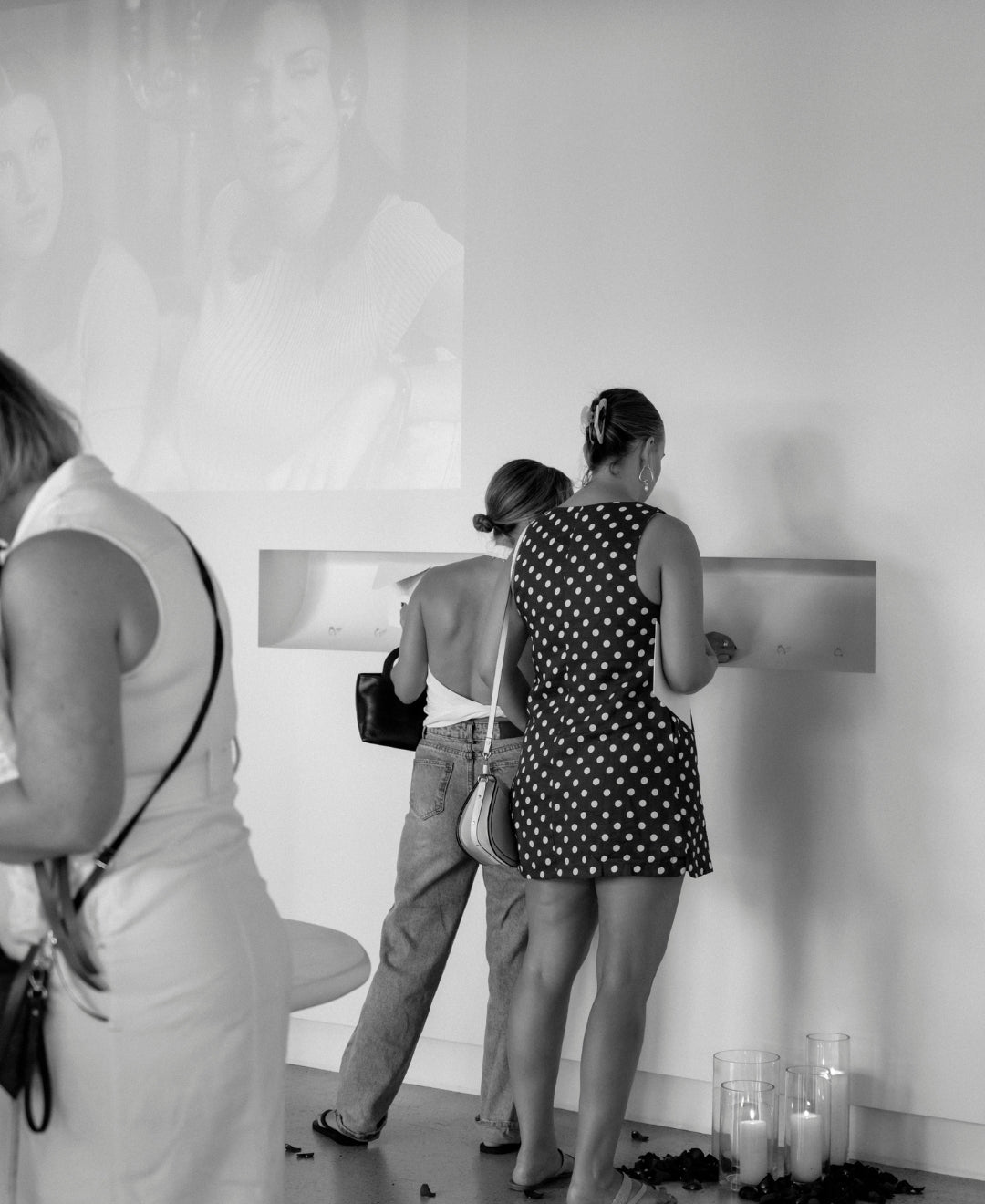 Women viewing jewellery display in a chic gallery setting with candles and a projected image on the wall, creating an elegant atmosphere.