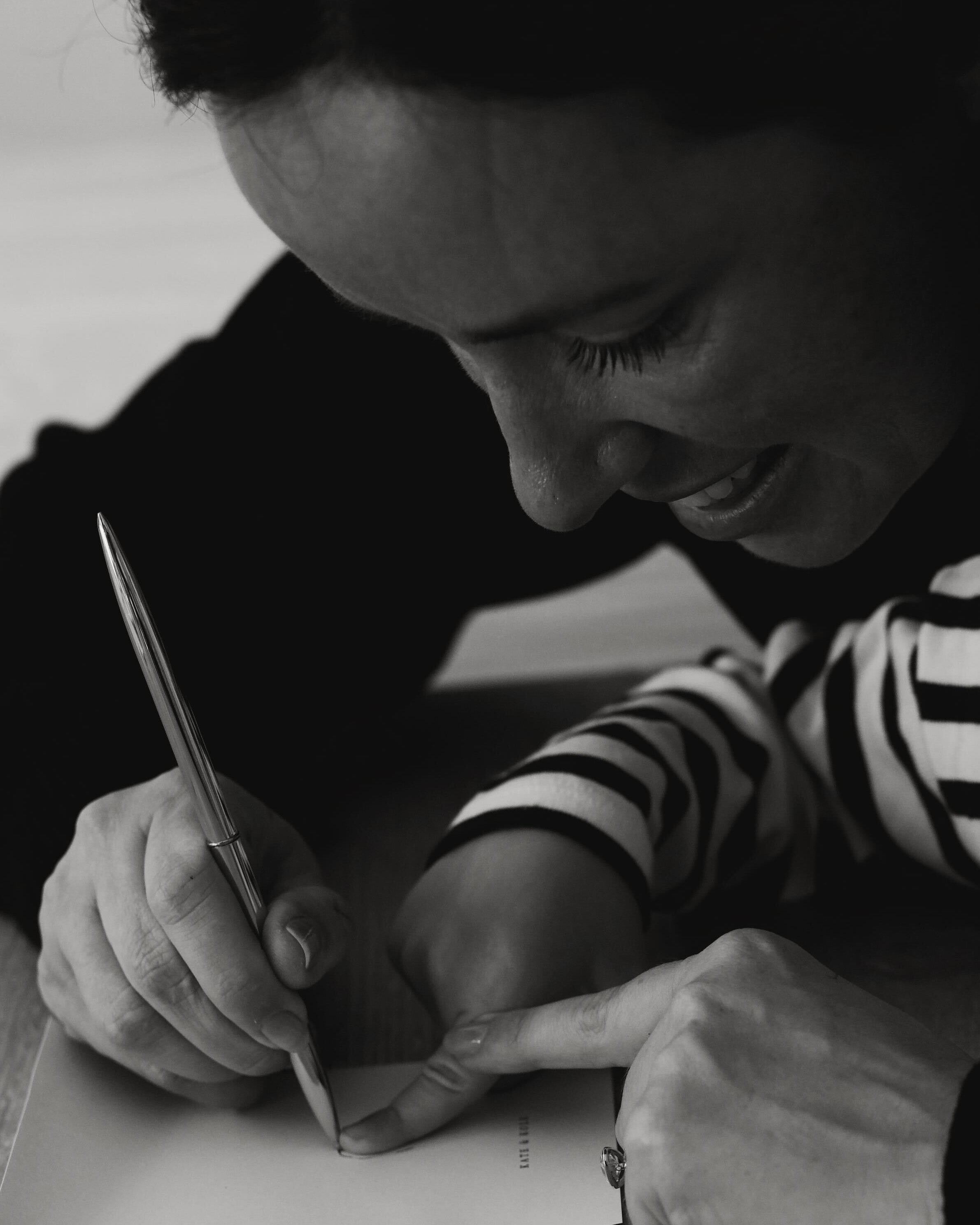 A woman in a striped shirt writes with a pen, showcasing a ring on her finger. Focus on jewellery craftsmanship and design.