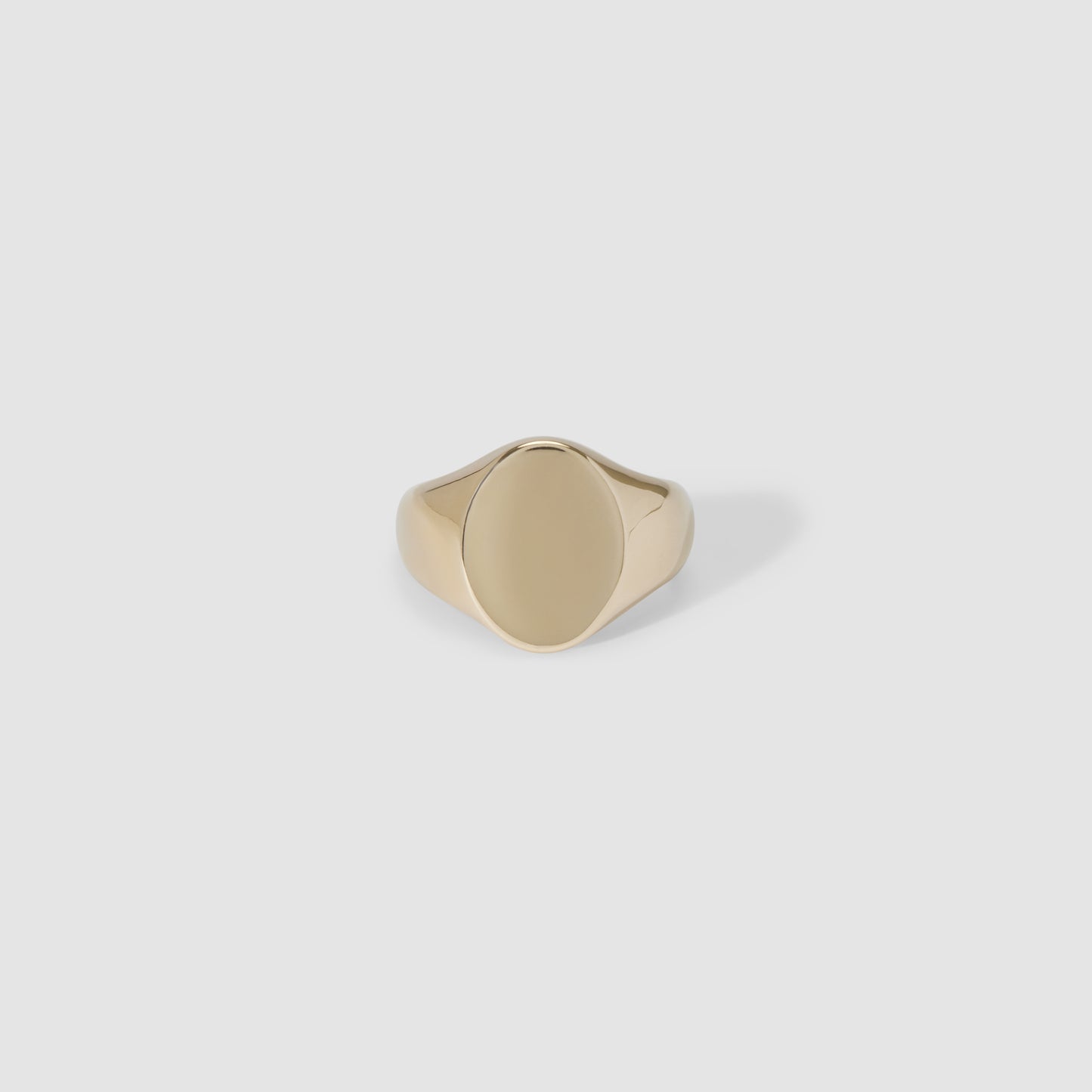 Gold signet ring with a smooth, oval face set against a light grey background, showcasing luxury jewellery design.