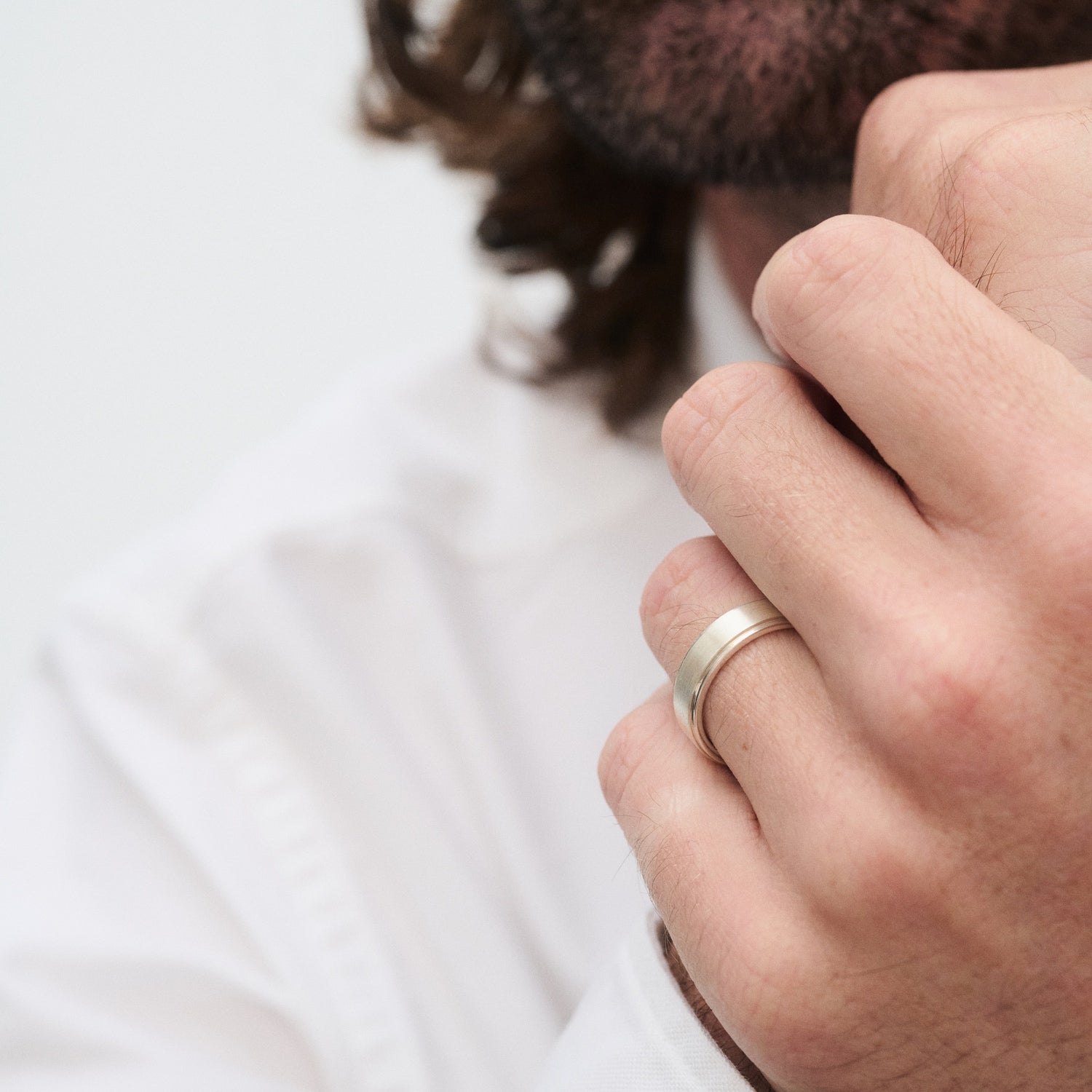 Man in white shirt with a silver wedding band on his ring finger, touching his chin thoughtfully. Luxurious jewellery focus.
