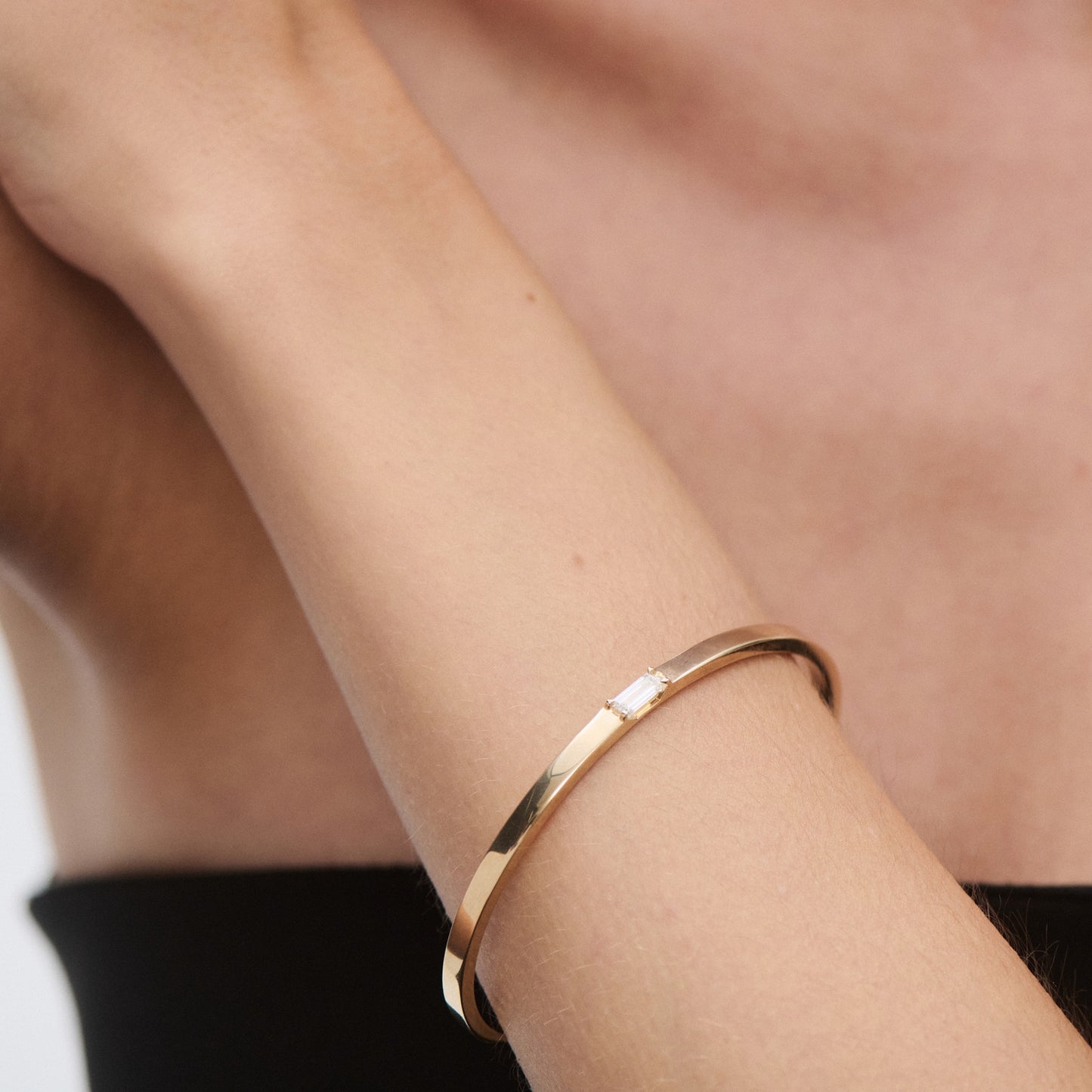 A close-up of a woman's arm wearing a sleek gold bangle with minimalist design, contrasted against a black garment.