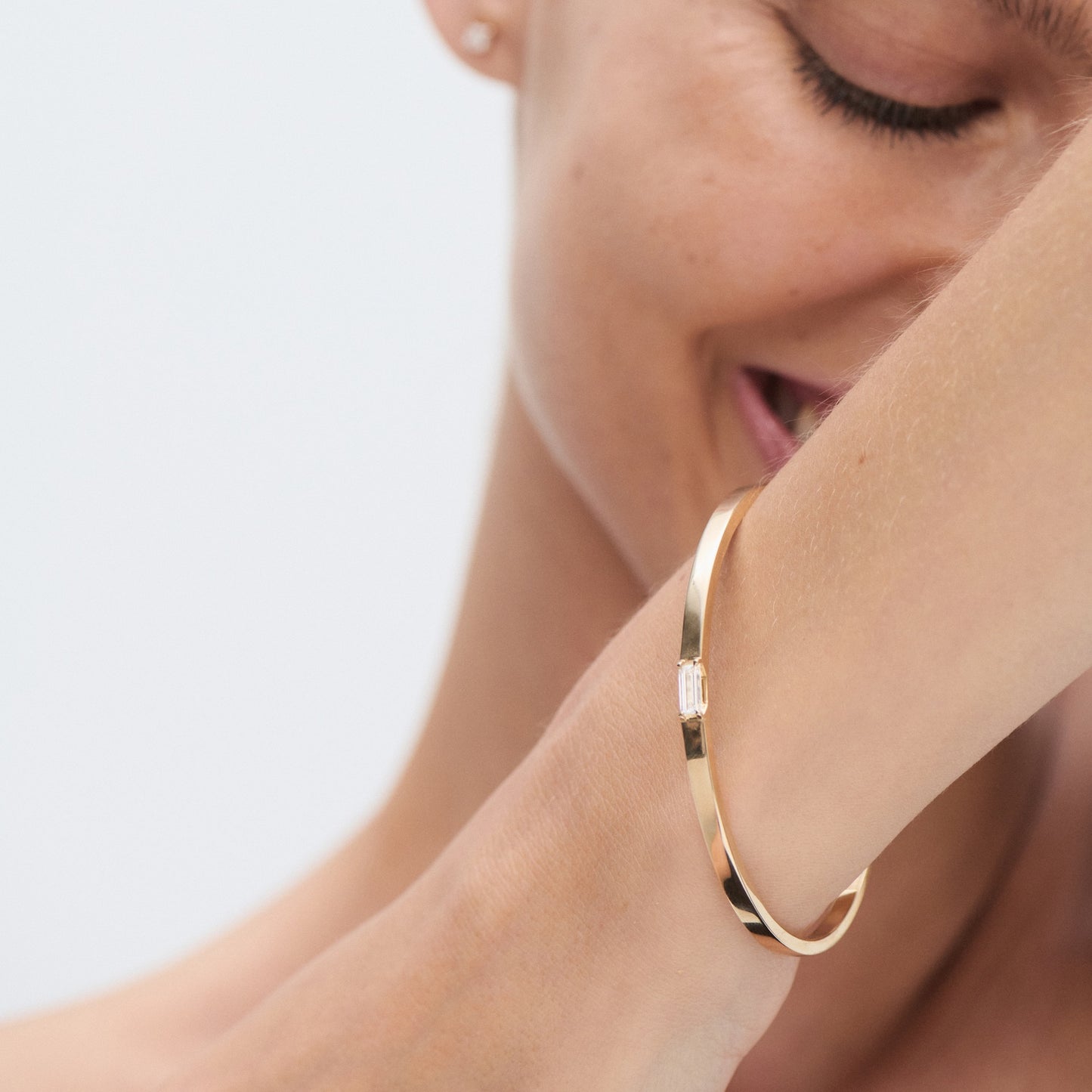 Smiling woman wearing an elegant gold bracelet with a rectangular gemstone, showcasing luxury jewellery.