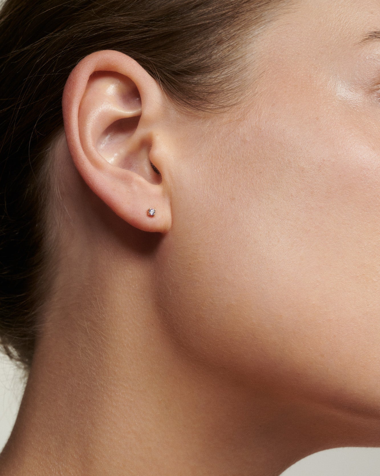 Close-up of a person wearing a small earring on a neutral background