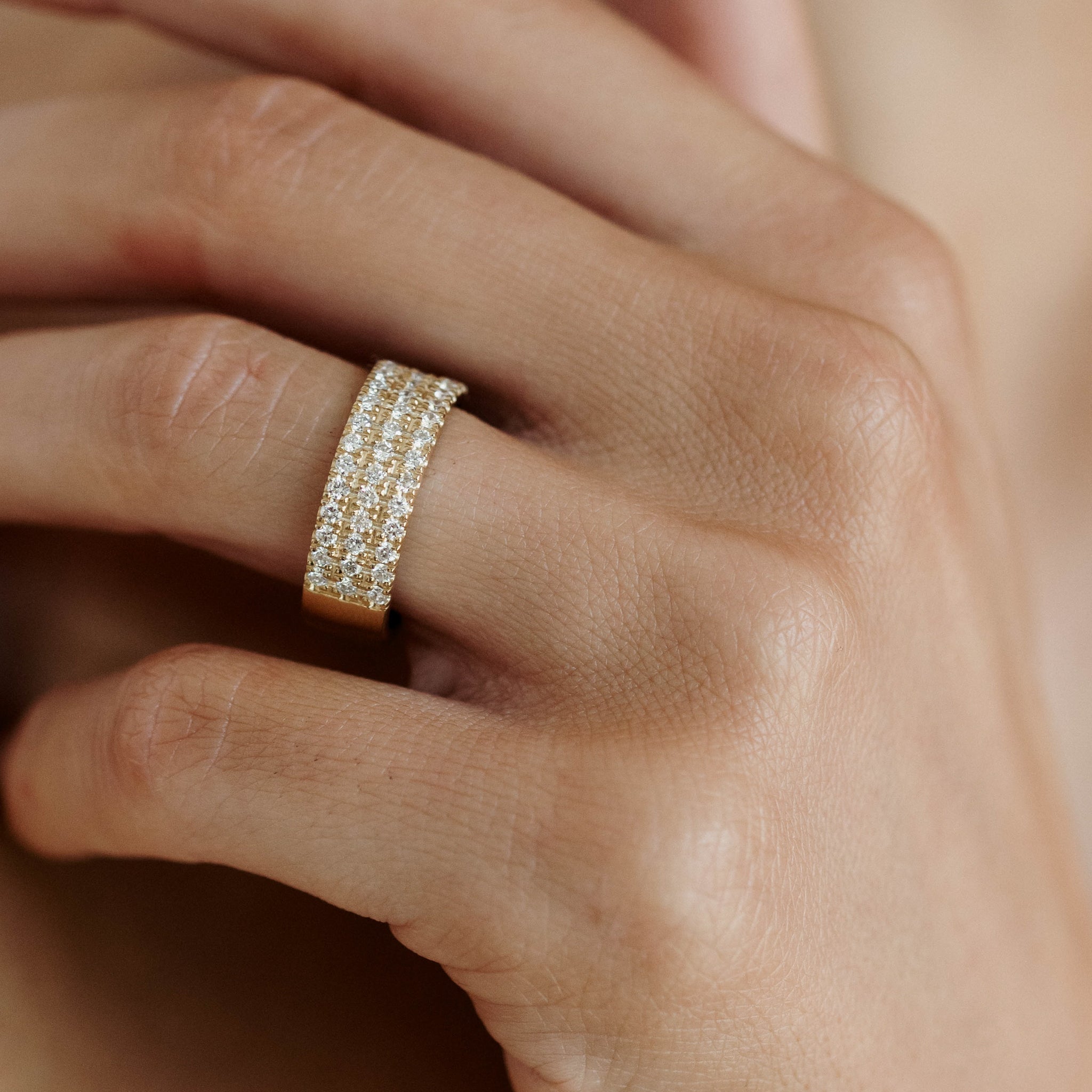 Close-up of a hand wearing an elegant gold ring with three rows of sparkling diamonds, showcasing luxury jewellery craftsmanship.
