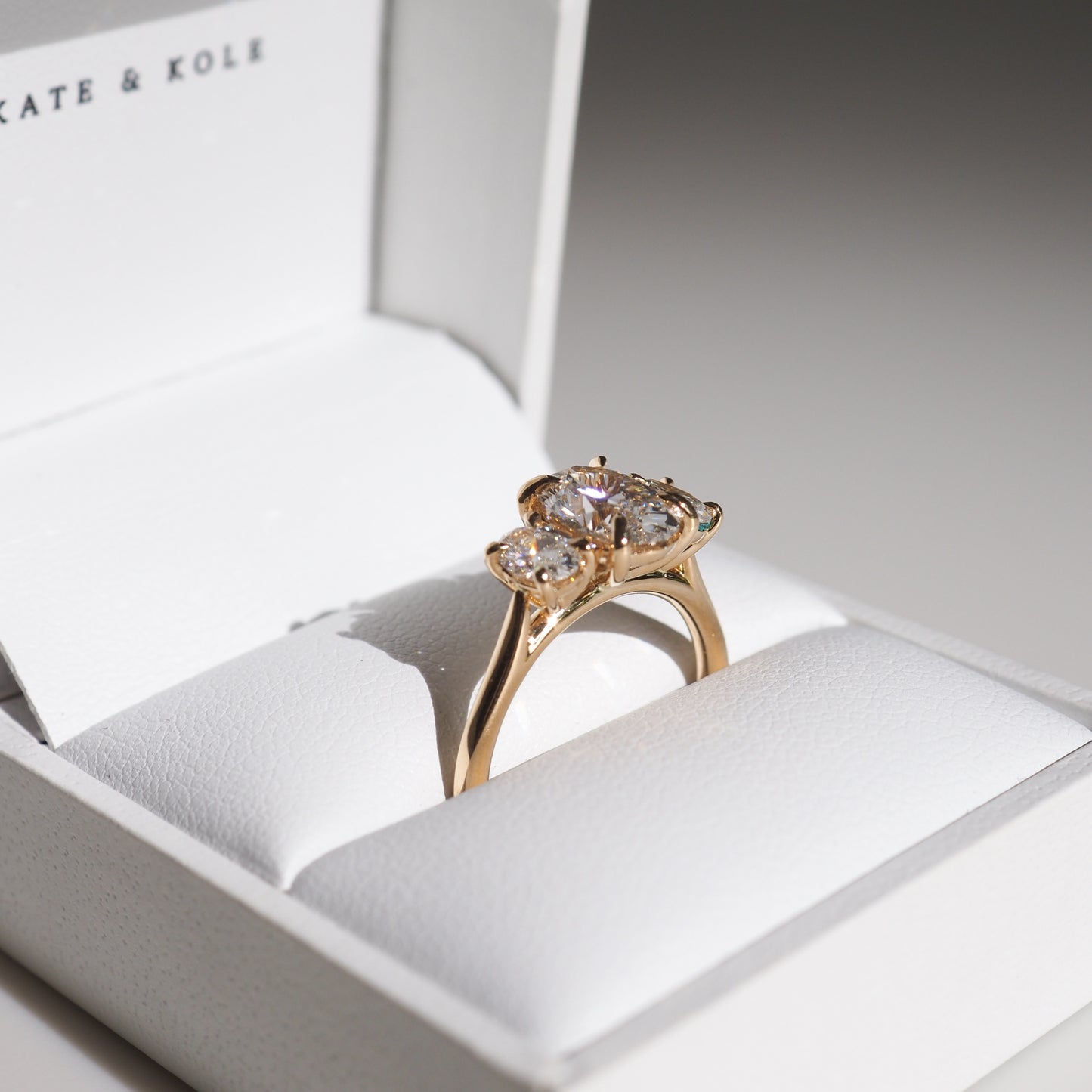 Elegant gold three-stone diamond ring in a white jewellery box, showcasing luxury design and craftsmanship.