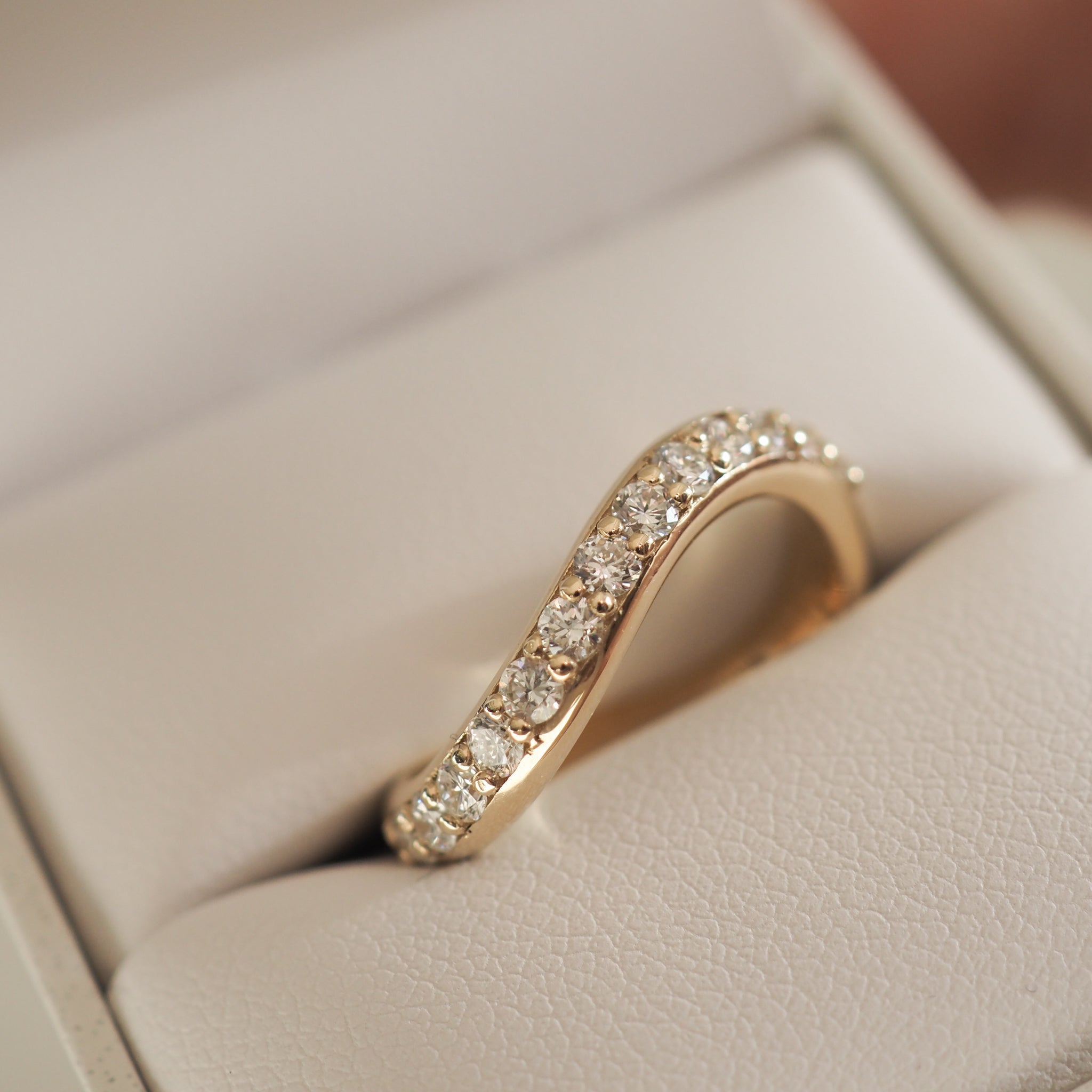 Gold band with sparkling diamonds set in a wave design, displayed in a beige jewellery box. Perfect for luxury bridal or anniversary gifts.