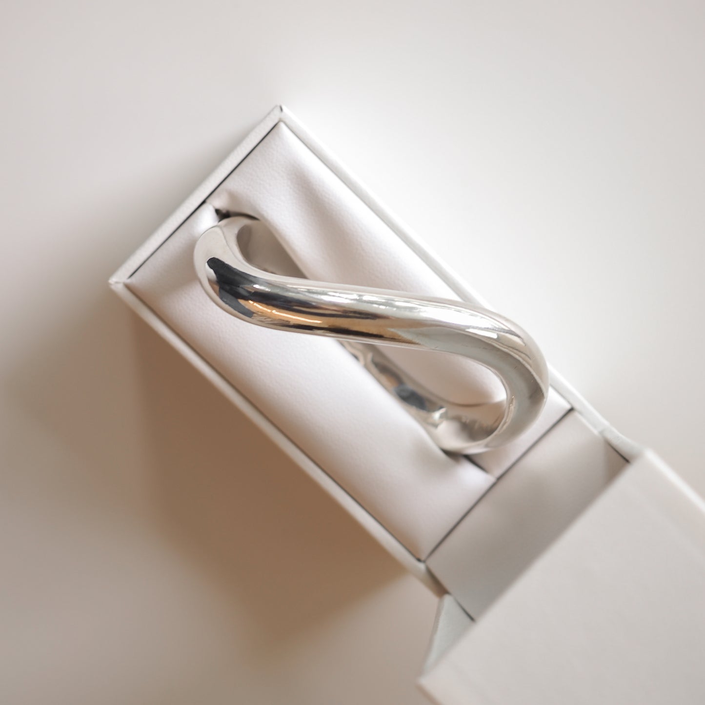 Elegant silver bracelet with a twisted design, presented in a minimalist white jewellery box on a light background.