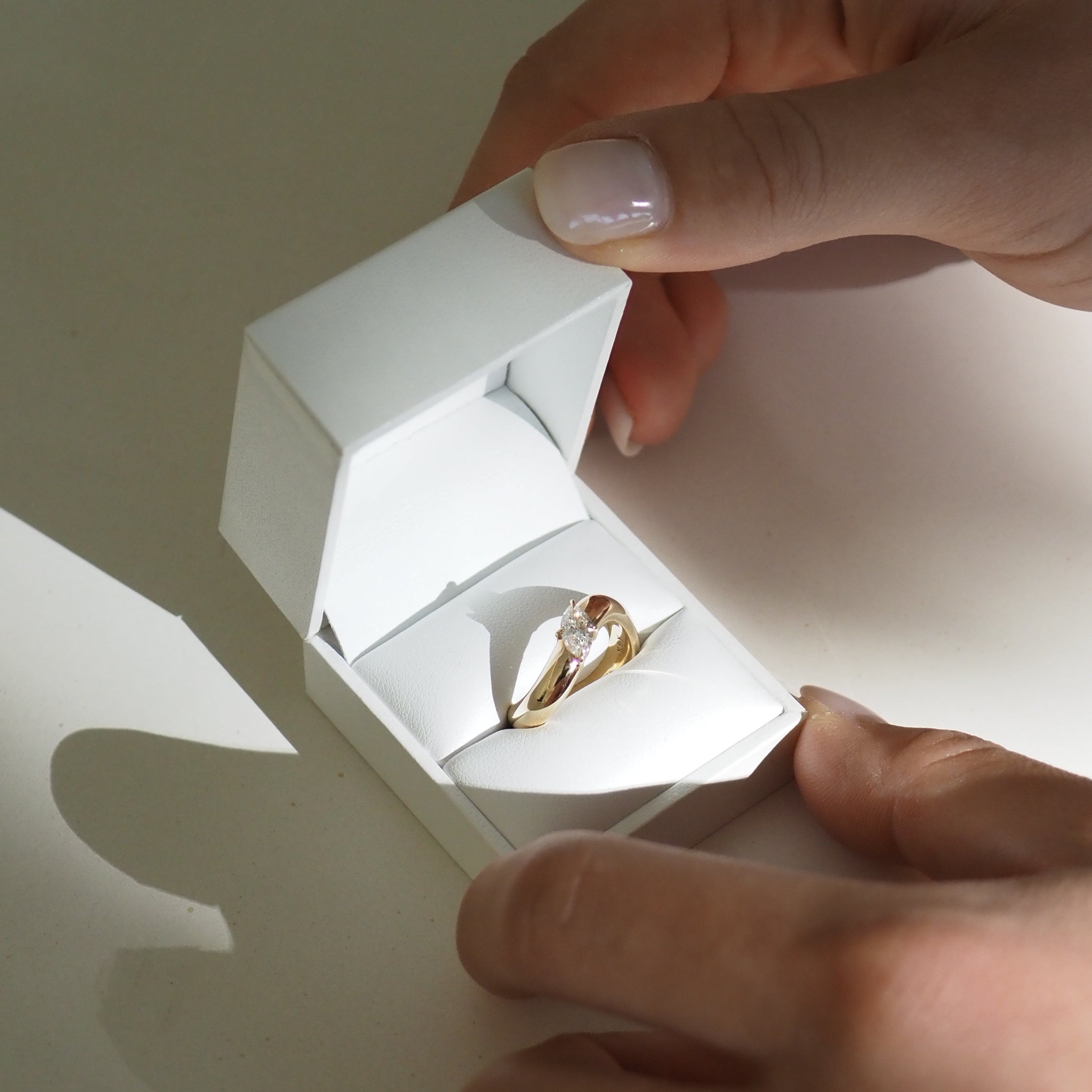 Hands holding a white box with a gold diamond engagement ring inside, highlighting luxury jewellery.