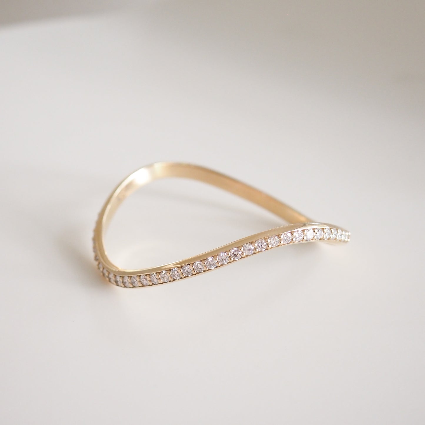 Elegant gold bracelet with a wavy design, adorned with sparkling diamonds, set against a soft white background. Perfect for luxury jewellery lovers.