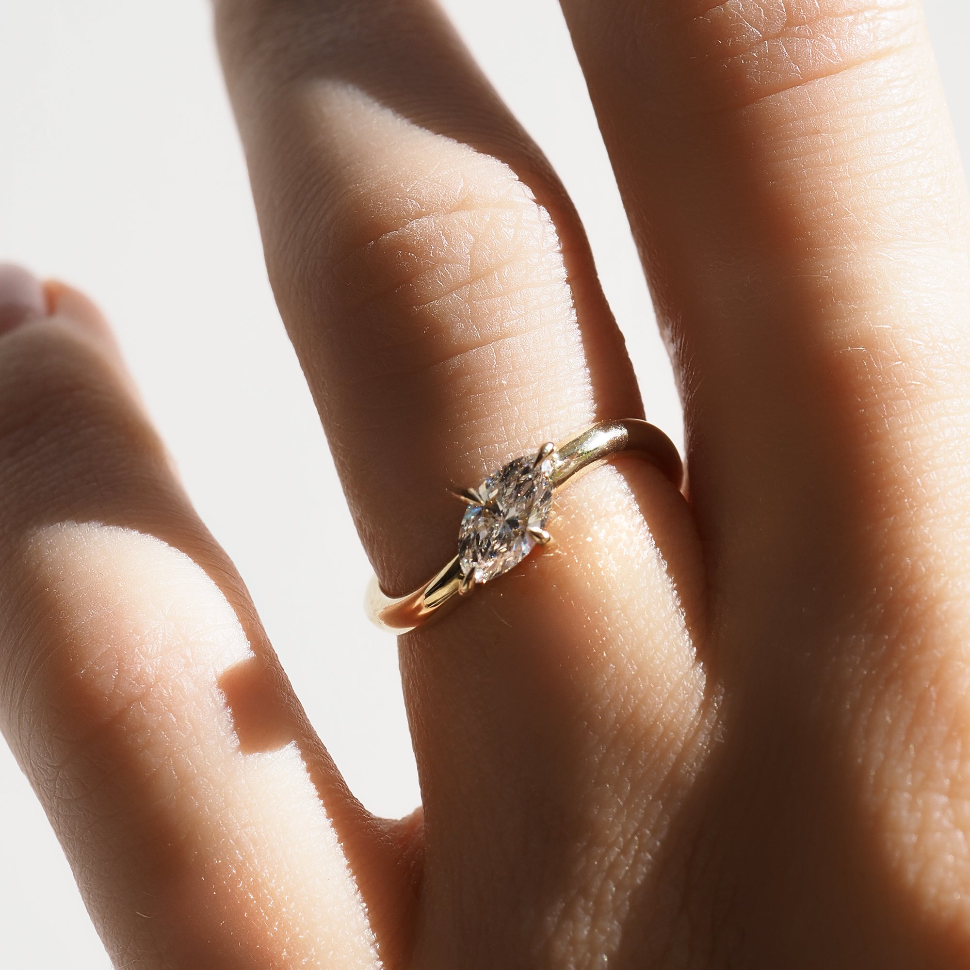 Close-up of a hand wearing a gold engagement ring with a sparkling oval-cut diamond, showcasing luxury jewellery in natural light.