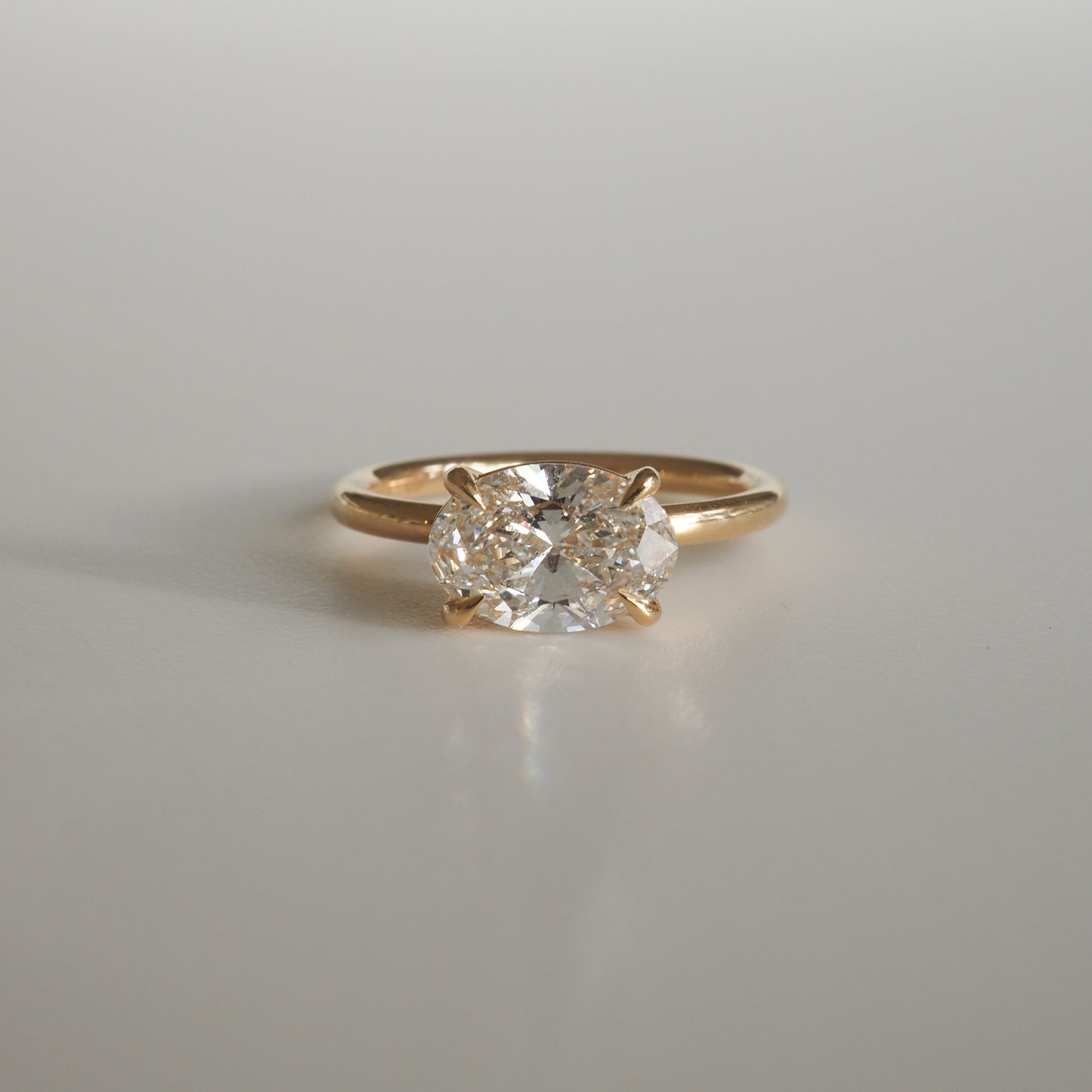 Gold band ring featuring an oval cut diamond, elegantly reflecting light on a plain surface, epitomising luxury jewellery.