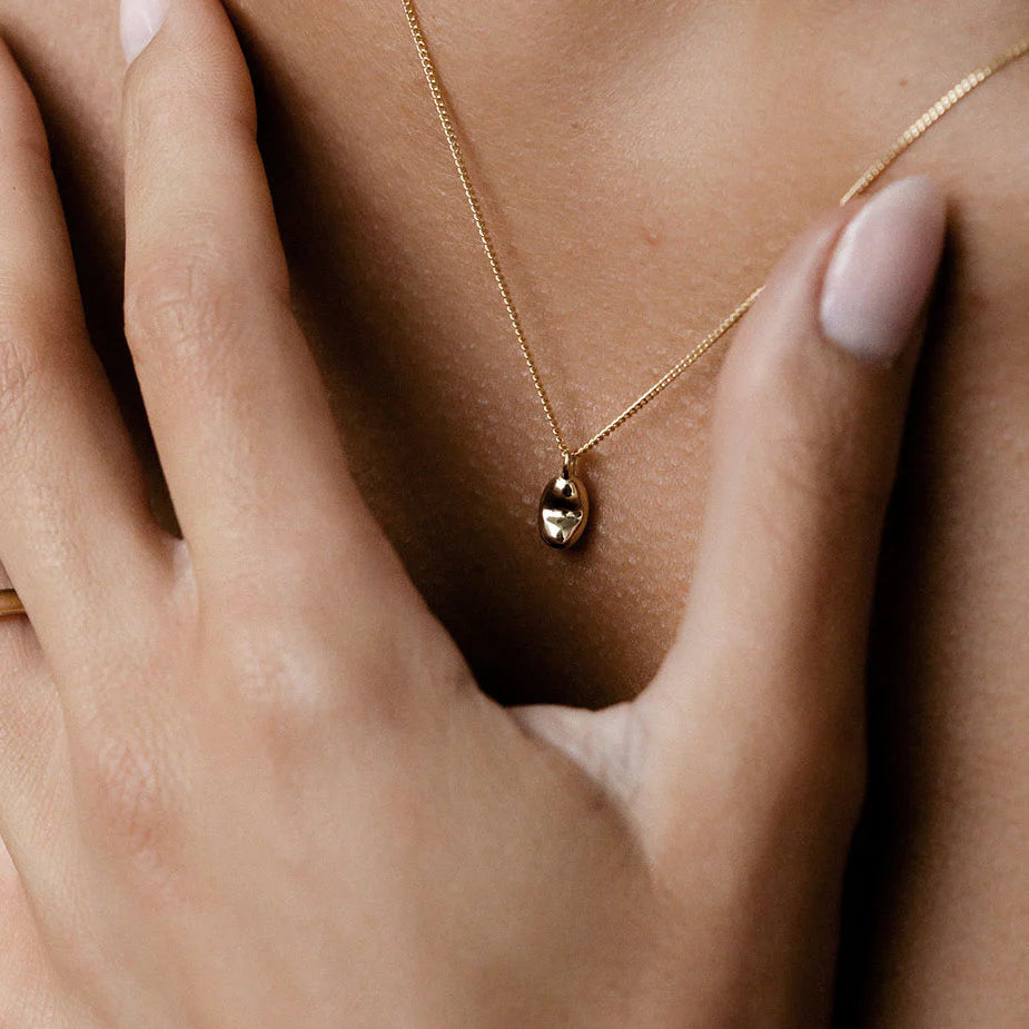 Close-up of a delicate gold pendant necklace on a woman's neck, with soft focus on her hand and polished nails, epitomising luxury jewellery.