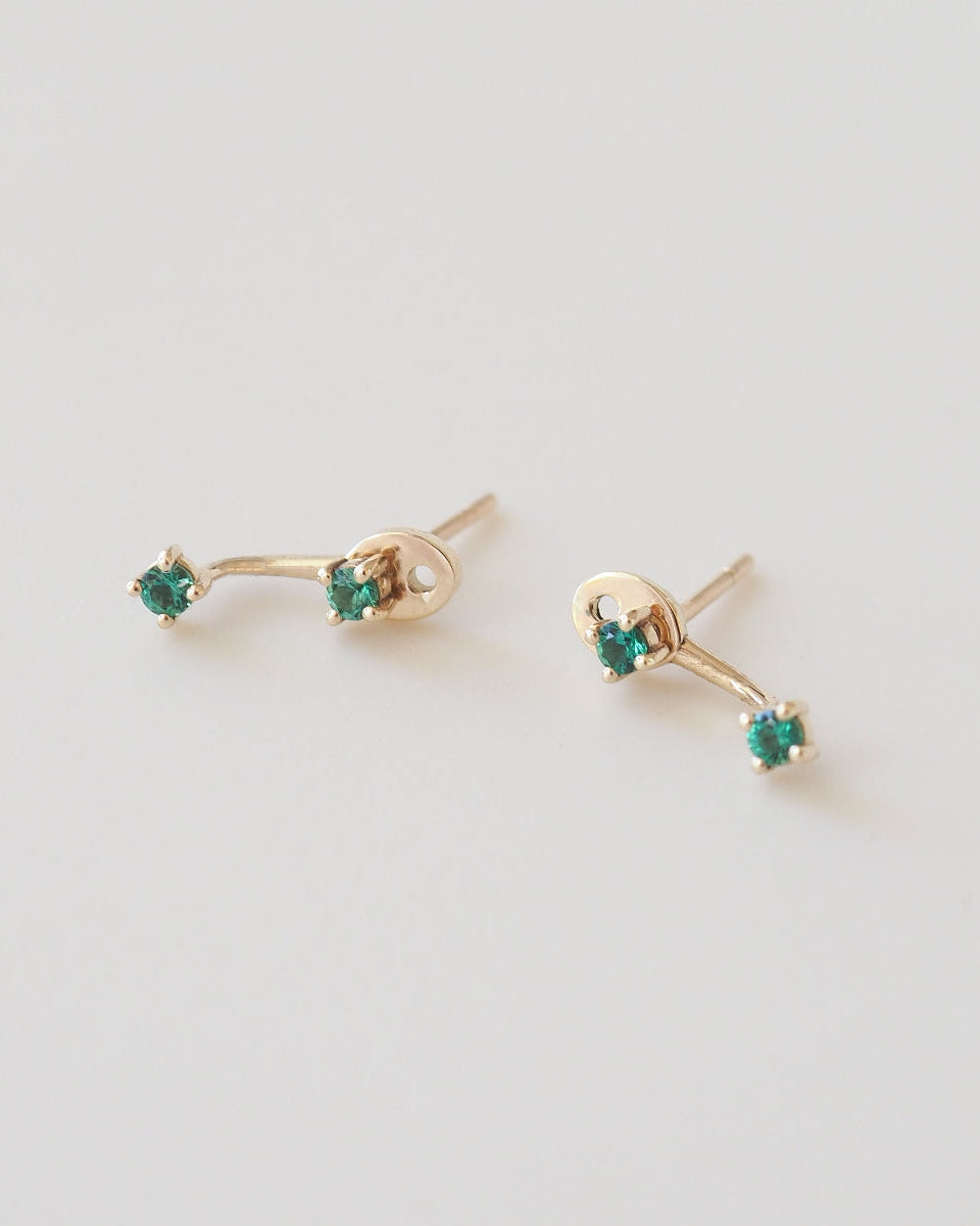 Gold earrings with green gemstones on a light gray background