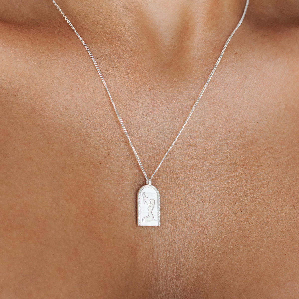 Silver necklace with an elegant pendant featuring an engraved feminine silhouette, showcased on a person's chest. Luxury jewellery design.