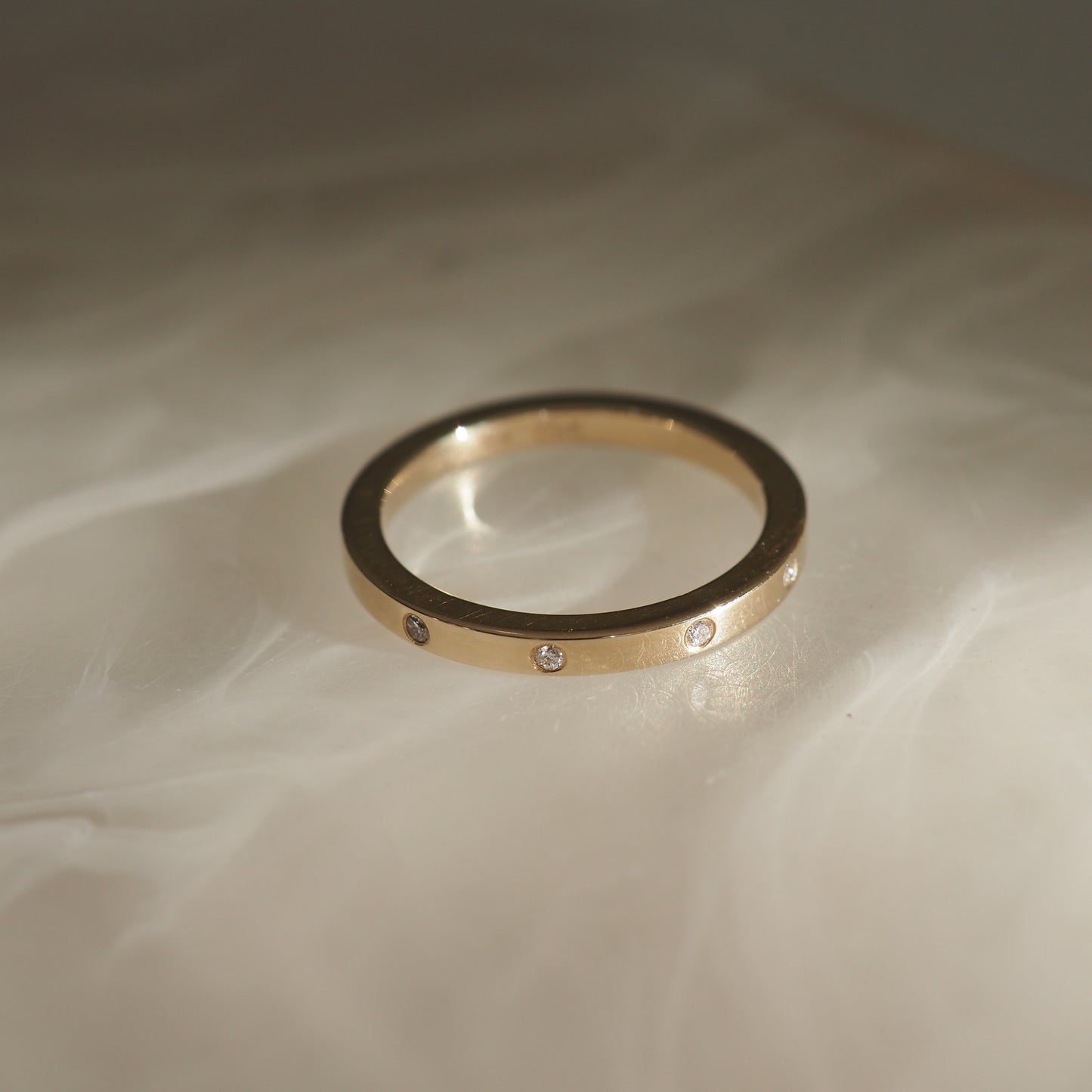 Gold ring with small embedded diamonds on a soft, white textured surface. Luxurious jewellery, elegant design.