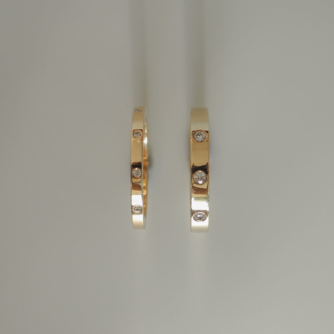 Two gold rings with embedded diamonds, showcasing elegant, minimalist design on a soft grey background. Perfect for luxury jewellery enthusiasts.