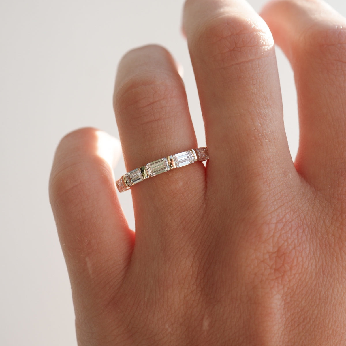 Hand wearing an elegant diamond baguette ring with a gold band, showcasing luxury jewellery. Soft lighting highlights the ring's brilliance.