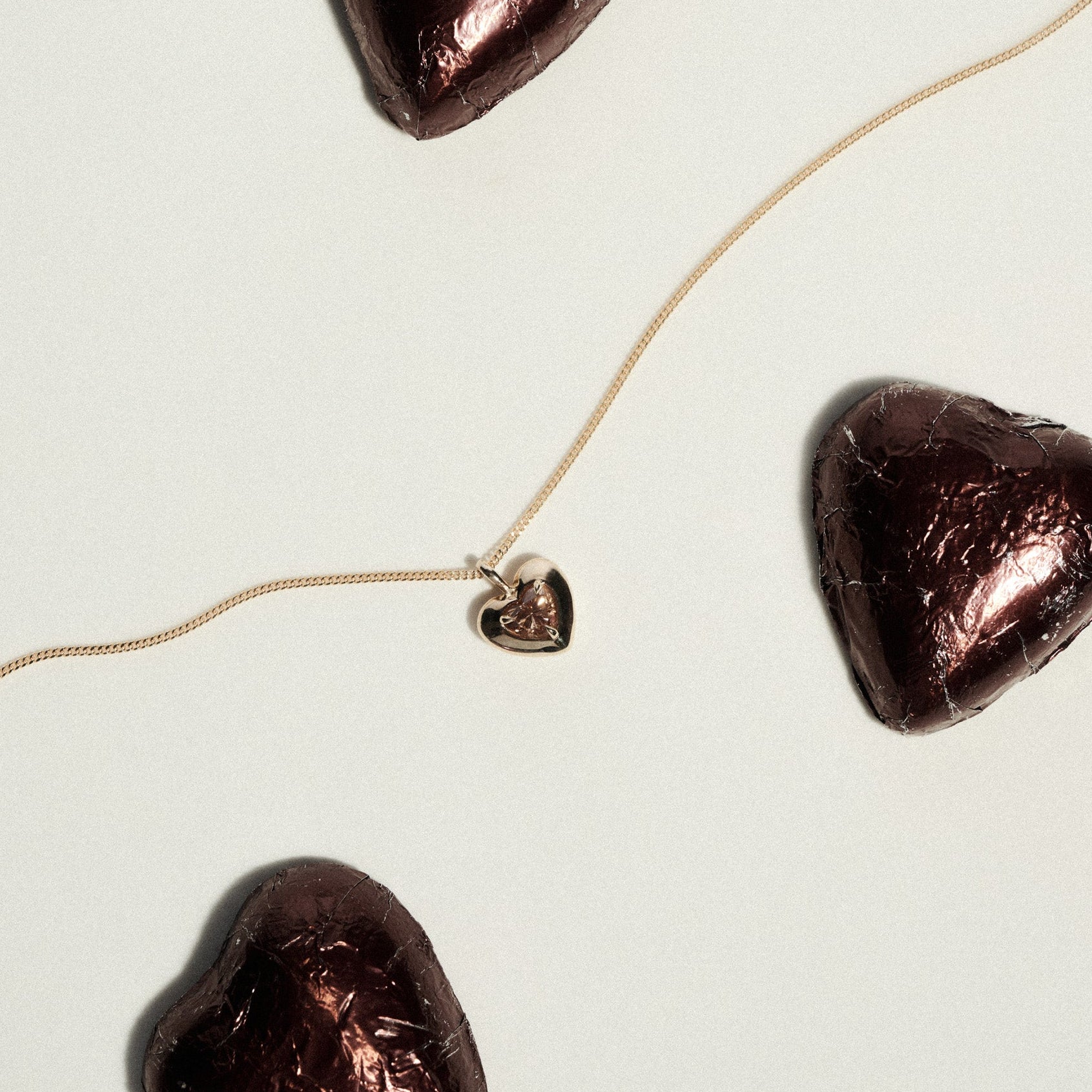 Heart-shaped chocolate pieces with a gold necklace draped on a light background