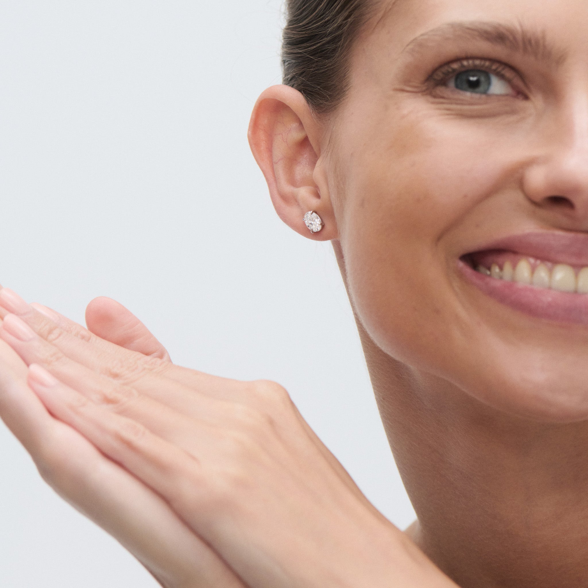 Woman with oval diamond earrings smiling and showing her hand against a light background
