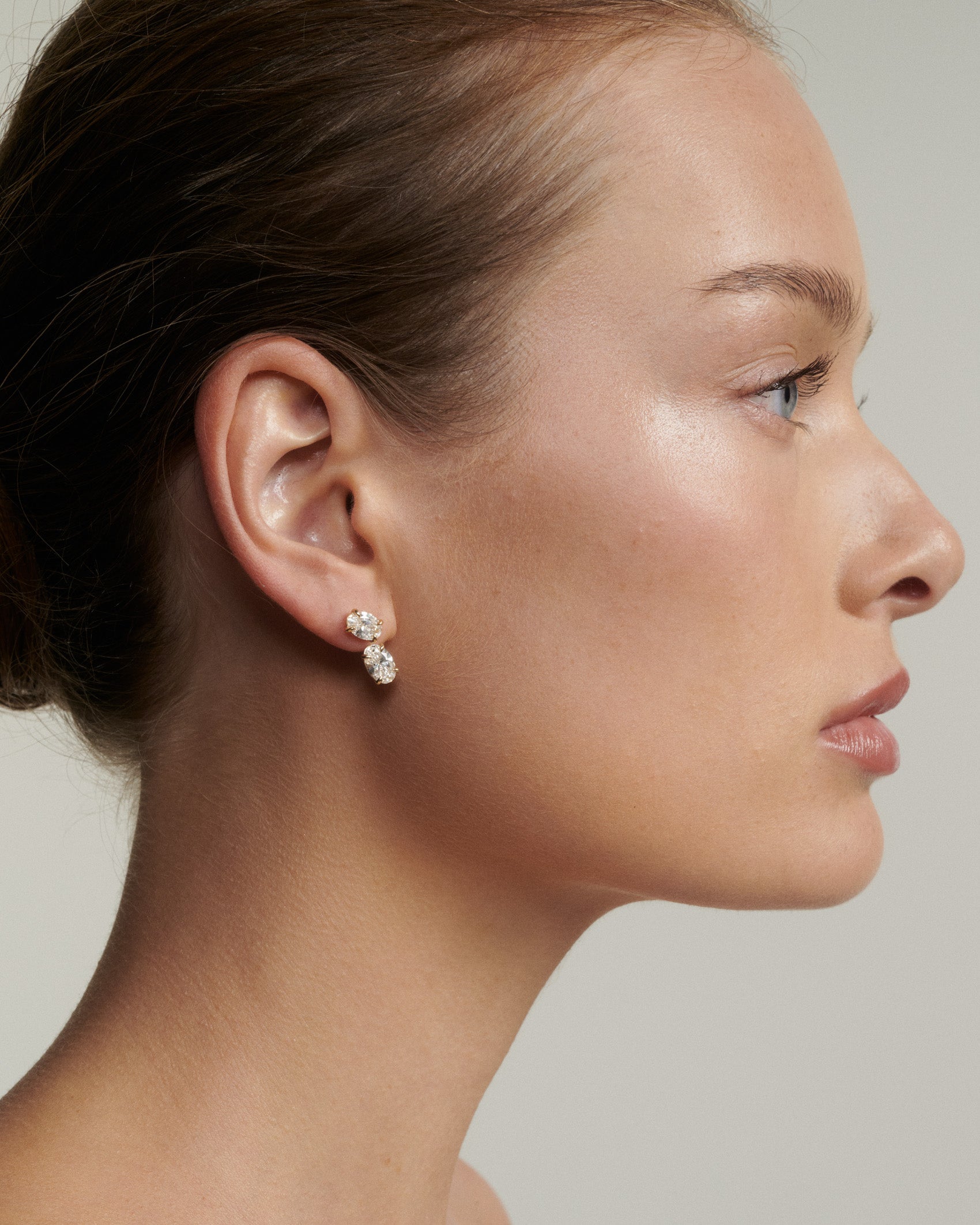 Side profile of a woman wearing diamond earrings against a neutral background