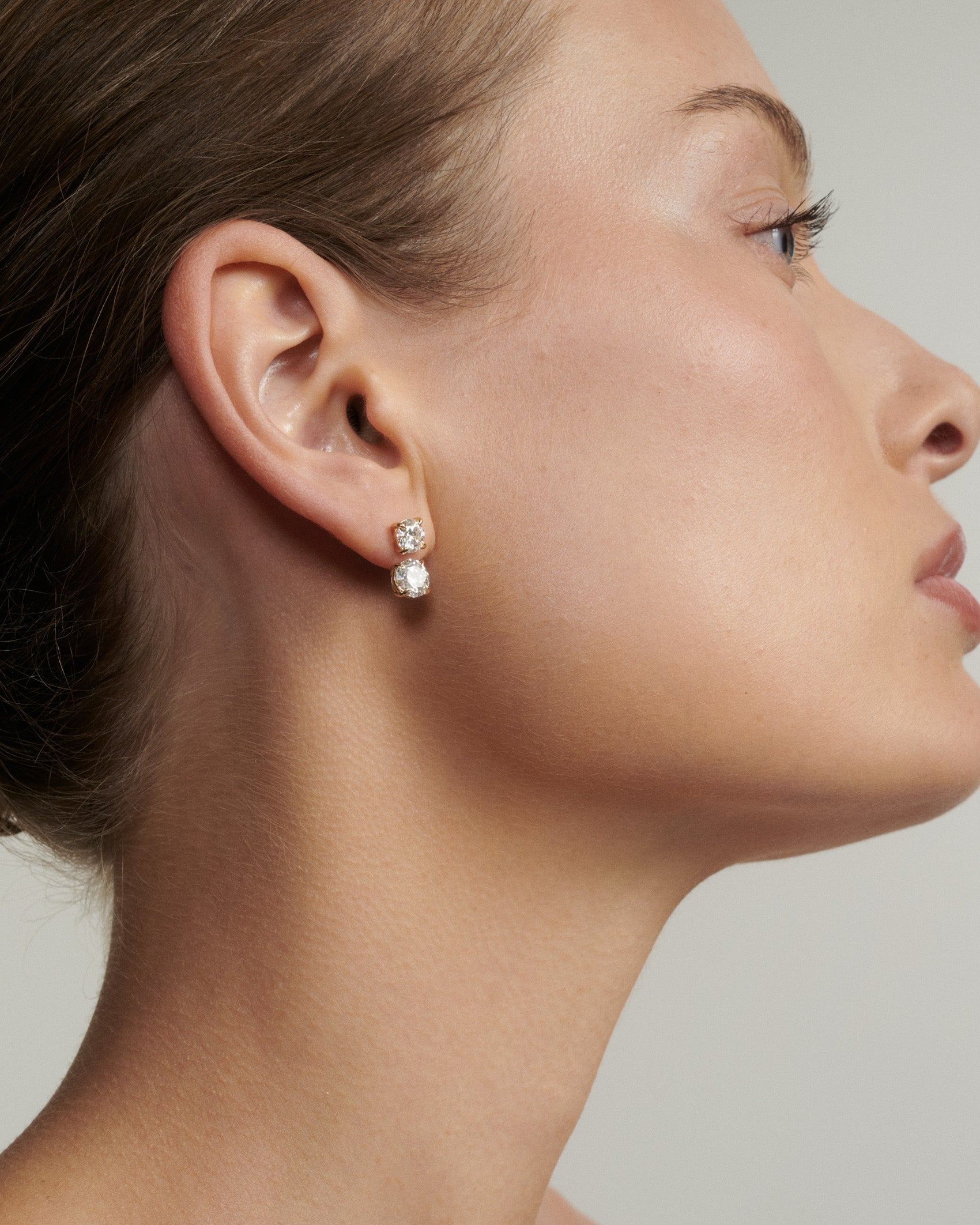Close-up of a woman wearing diamond earrings against a neutral background